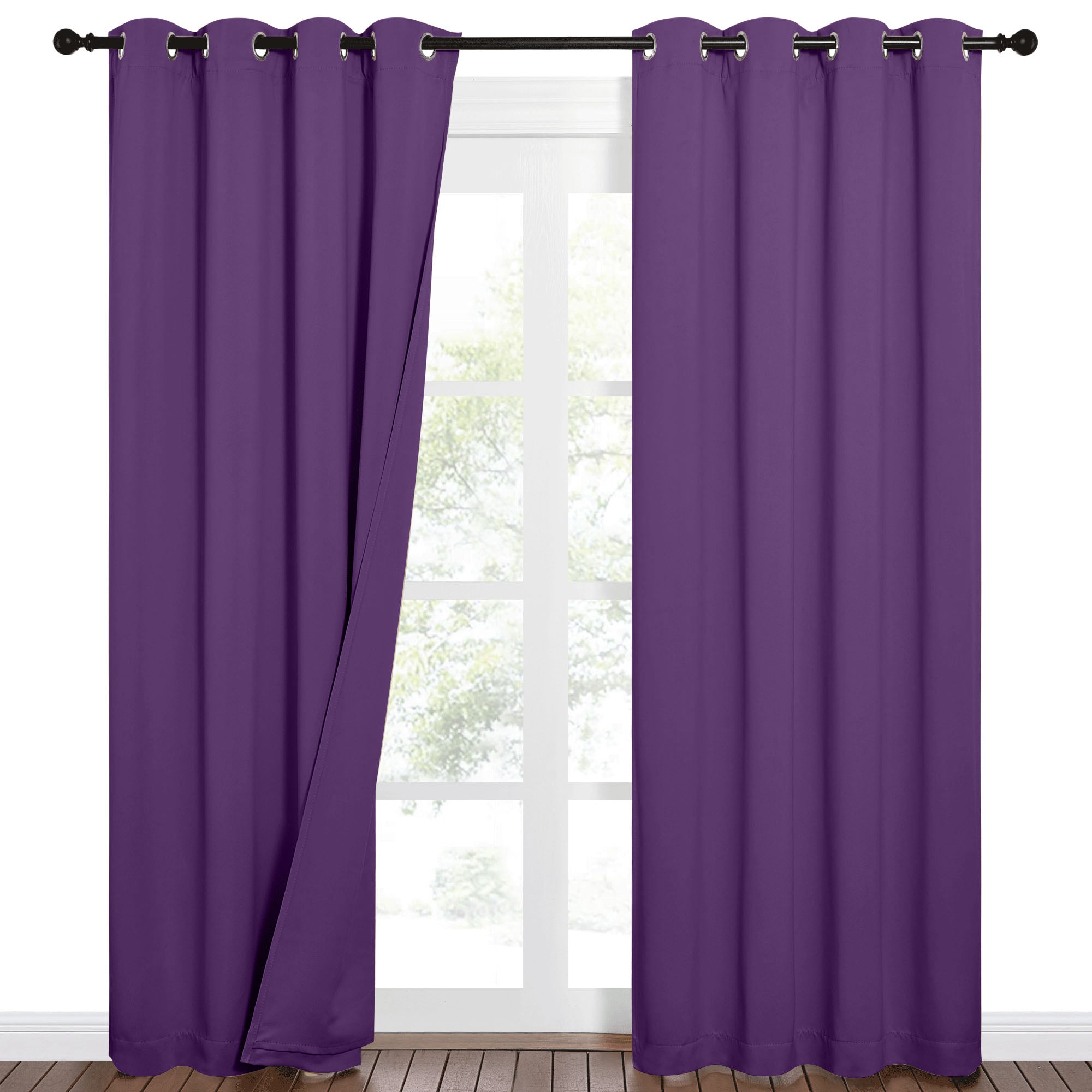 A pair of deep purple Sound Barrier 100% blackout grommet curtains, one panel open to reveal a window and wood floor.
