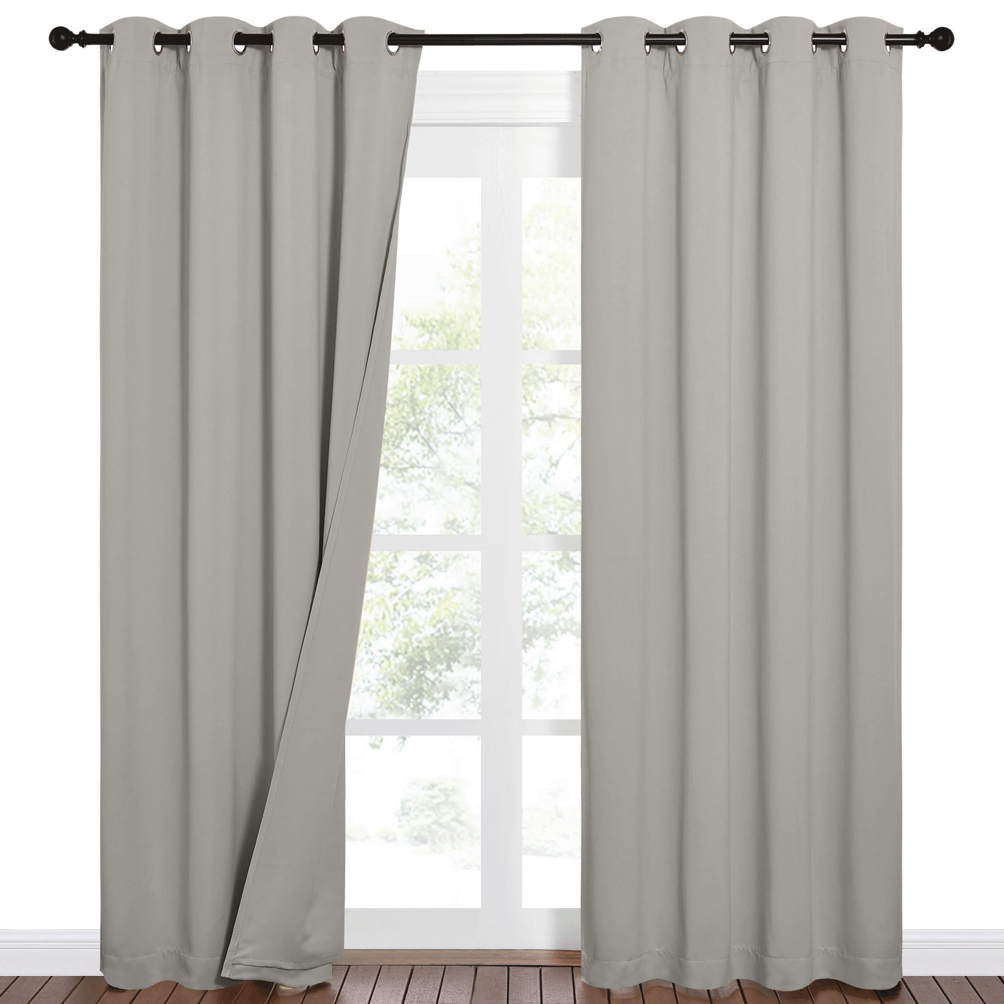 Grey sound barrier blackout curtains with grommet top on a window. One panel is slightly open, revealing trees outside.