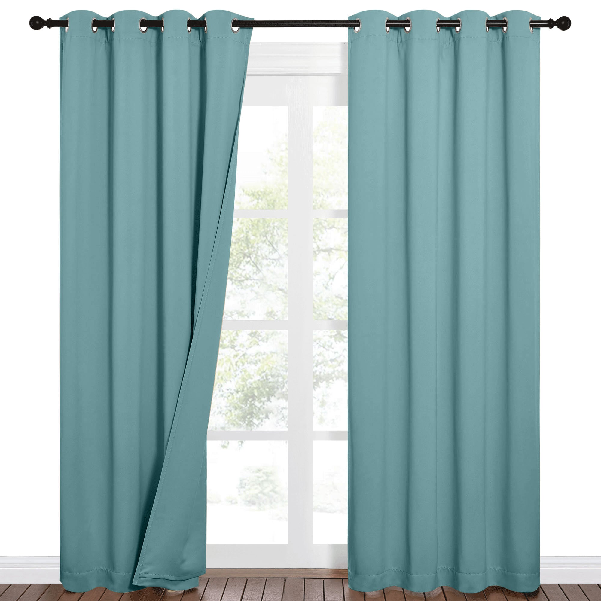 Two teal blackout grommet curtains on a black rod, one pulled back revealing a window and outdoor trees.