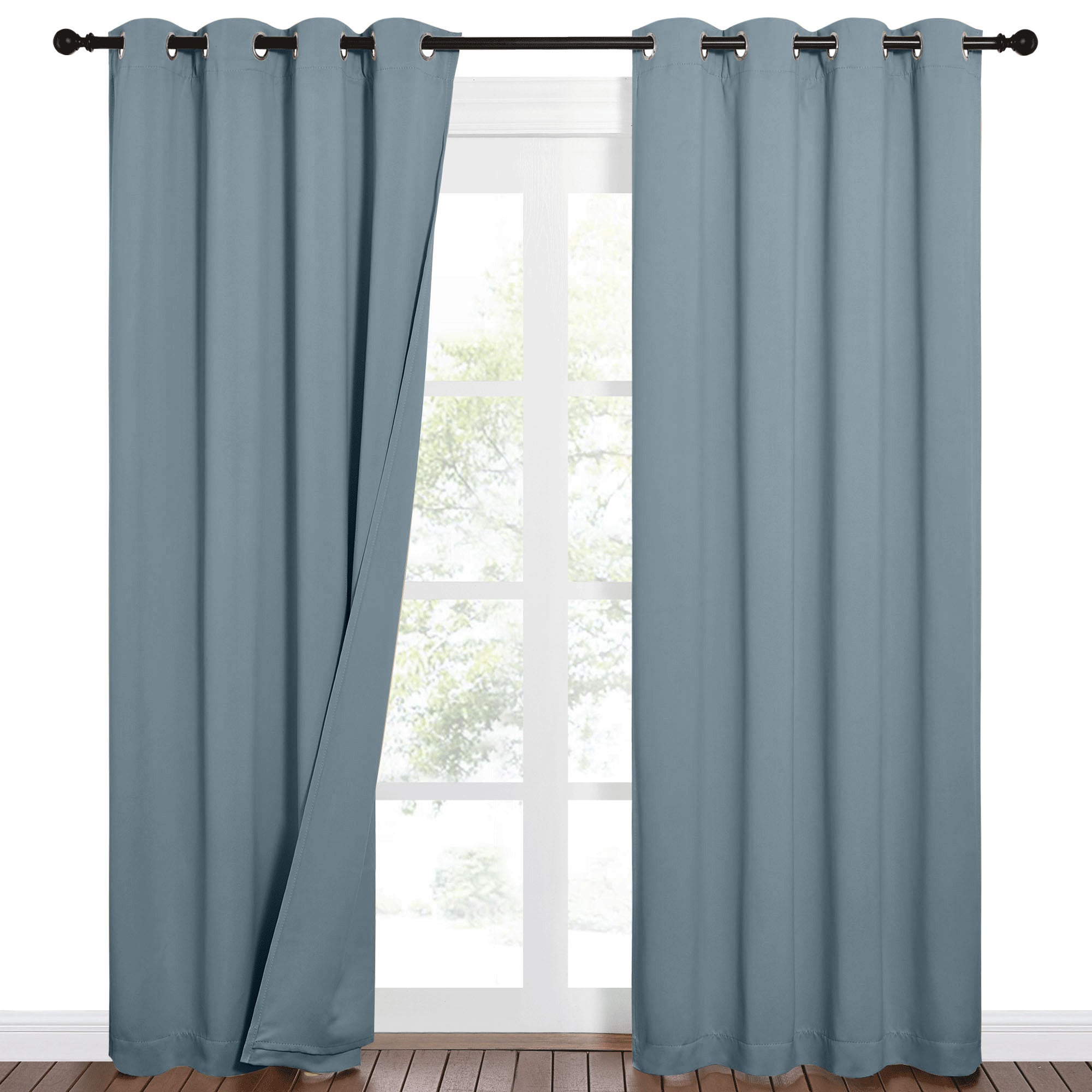 Partially open blue-grey 100% blackout curtains with grommet tops on a black rod, revealing a window and outdoor view.
