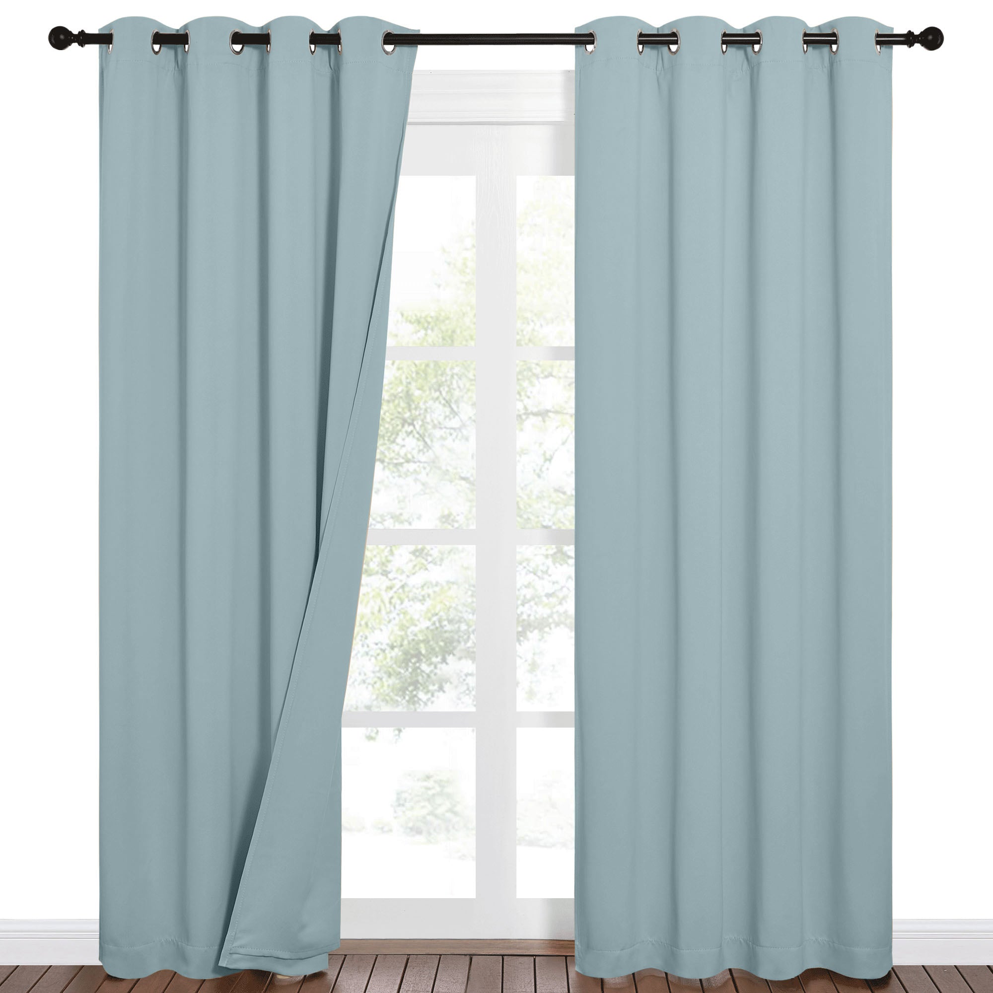 Pair of light blue blackout grommet curtains on a black rod, one panel fully closed and the other slightly open by a window.