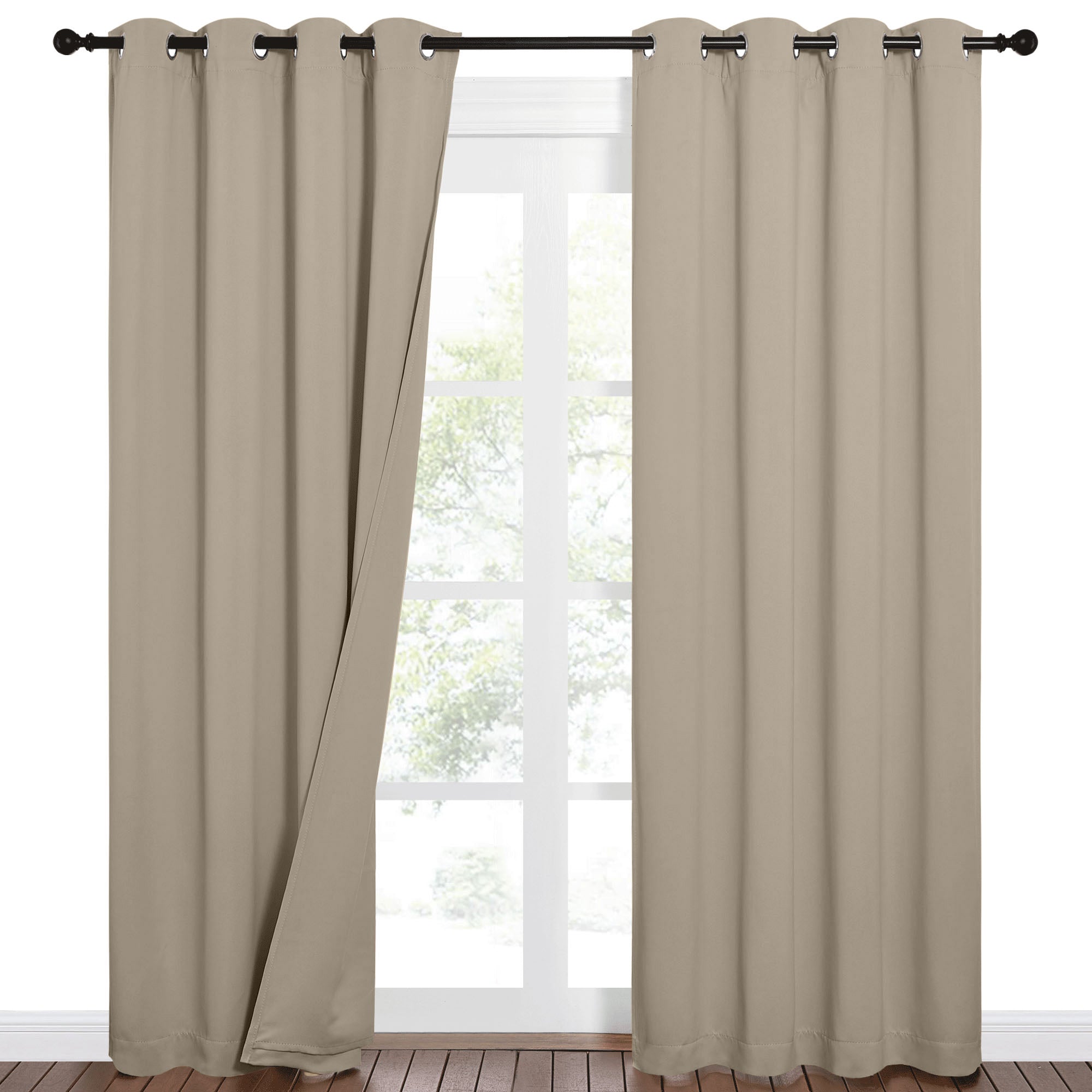 Two beige grommet blackout curtains on a black rod, one panel slightly open over a window with outdoor trees.
