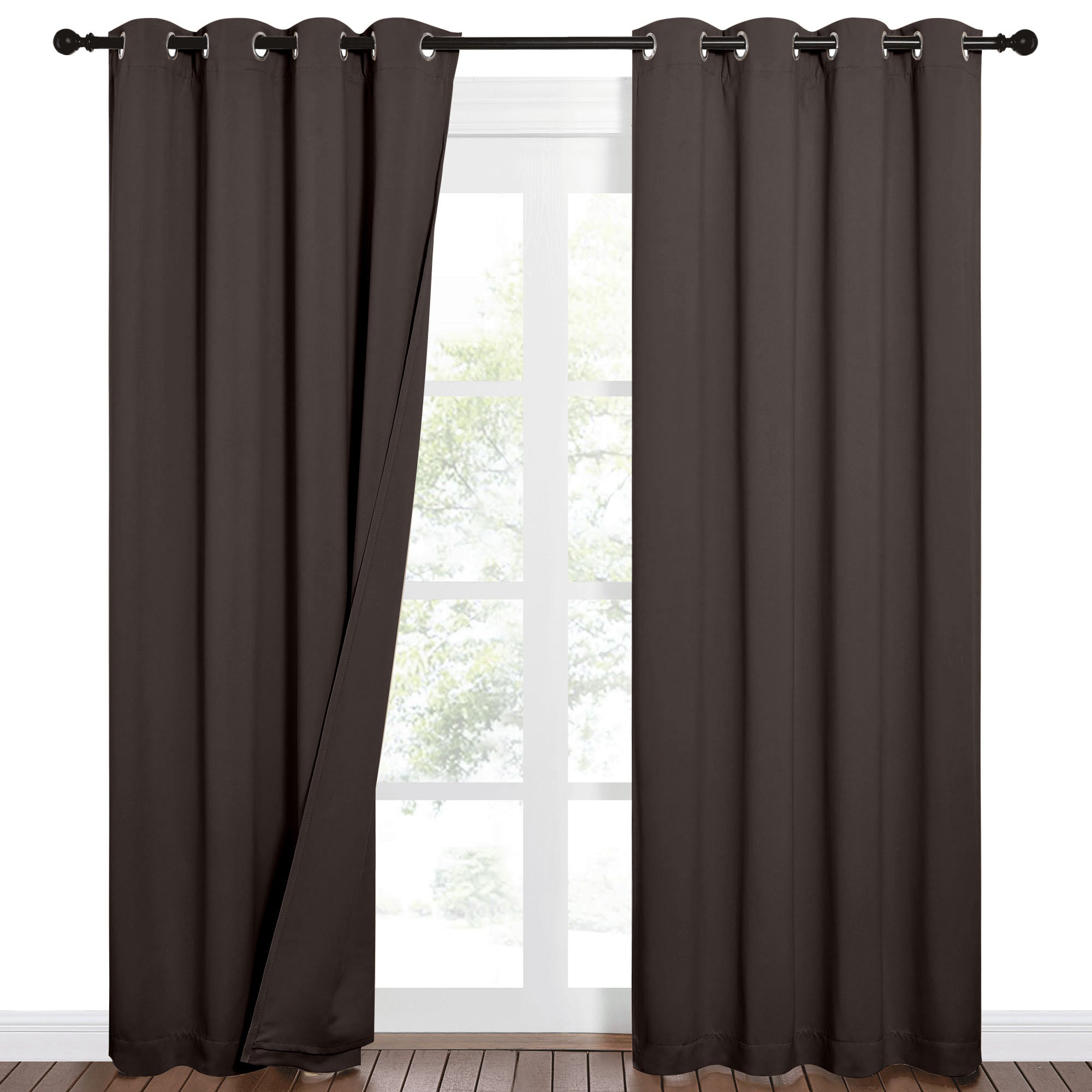 Deep brown 100% blackout grommet curtains on a rod, partially open over a window revealing green trees outside.