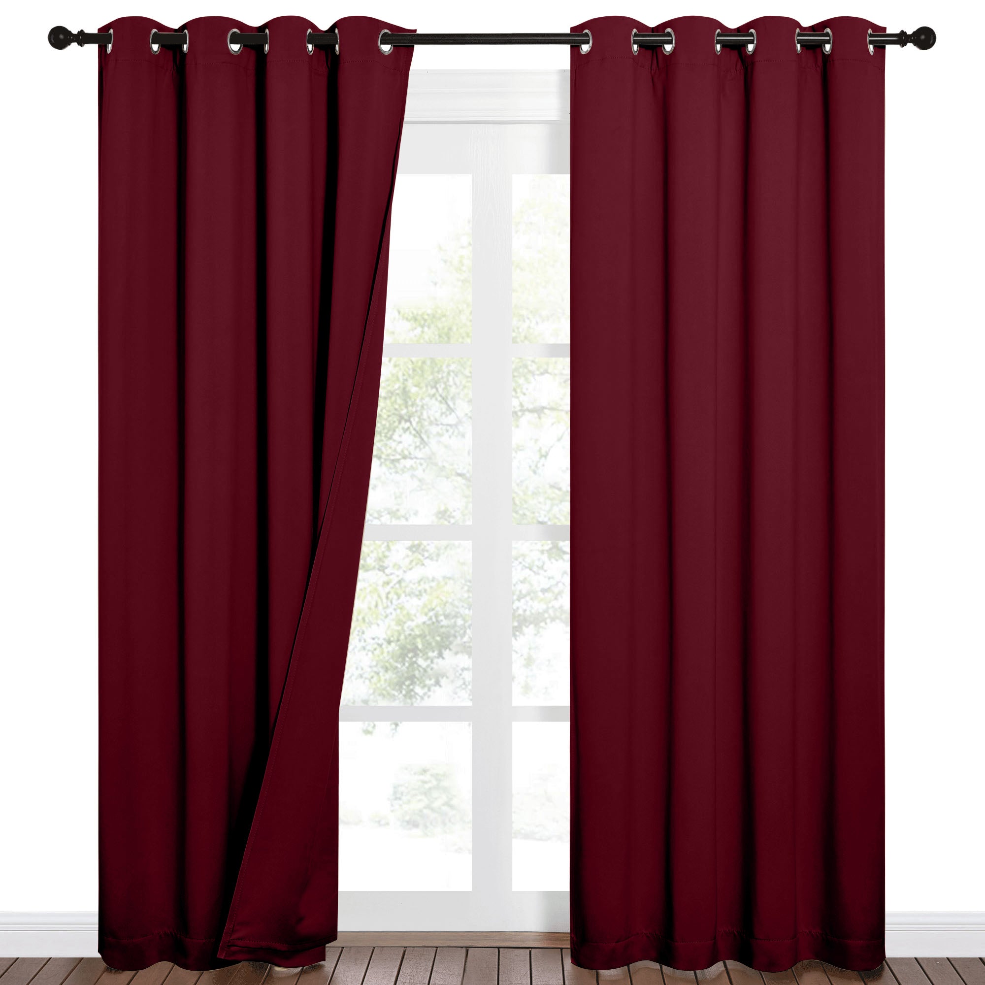 Pair of burgundy sound barrier 100% blackout curtains with grommets, partially open on a window showing trees outside.