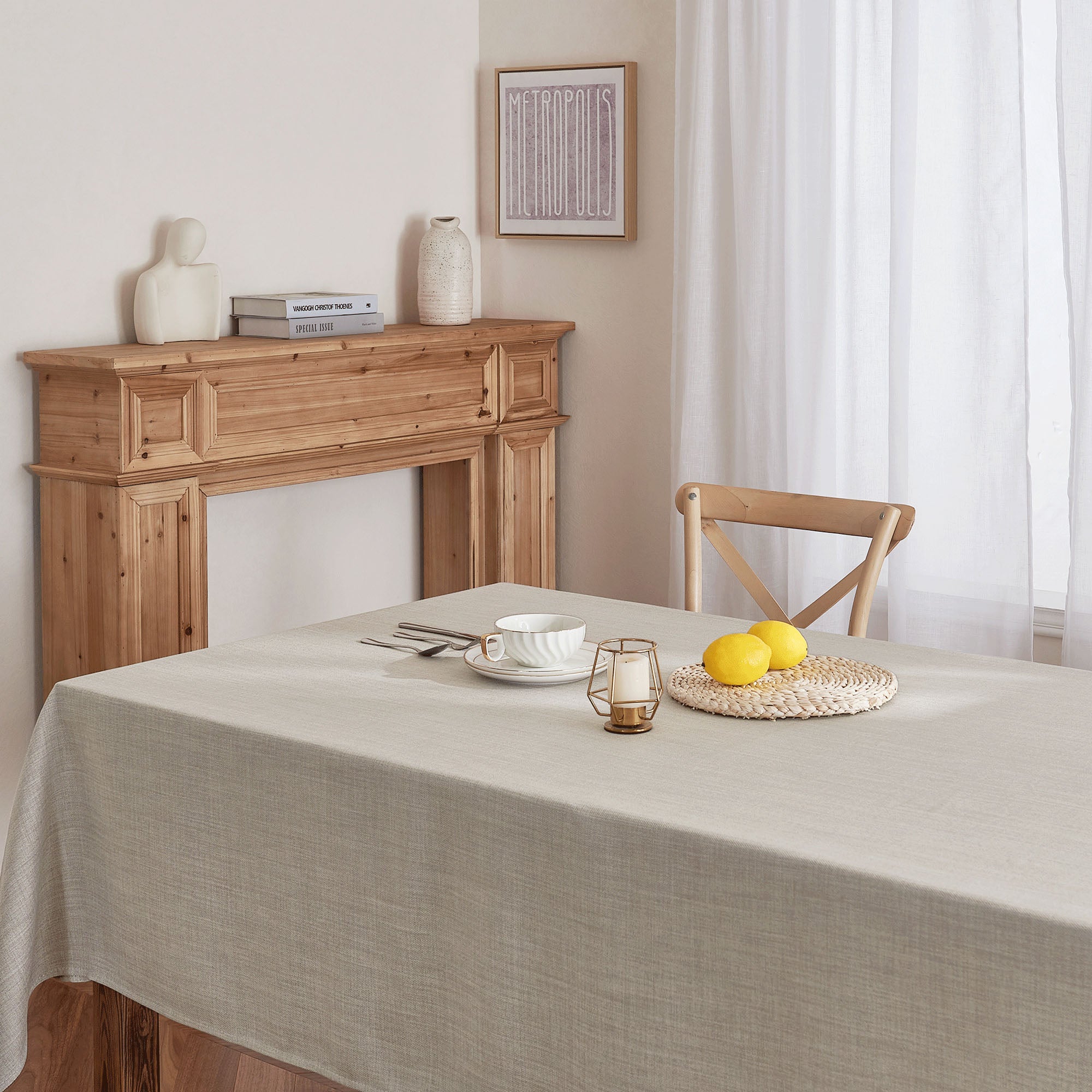 Light gray linen tablecloth covering a dining table, set with a teacup, silverware, lemons, and a candle holder.