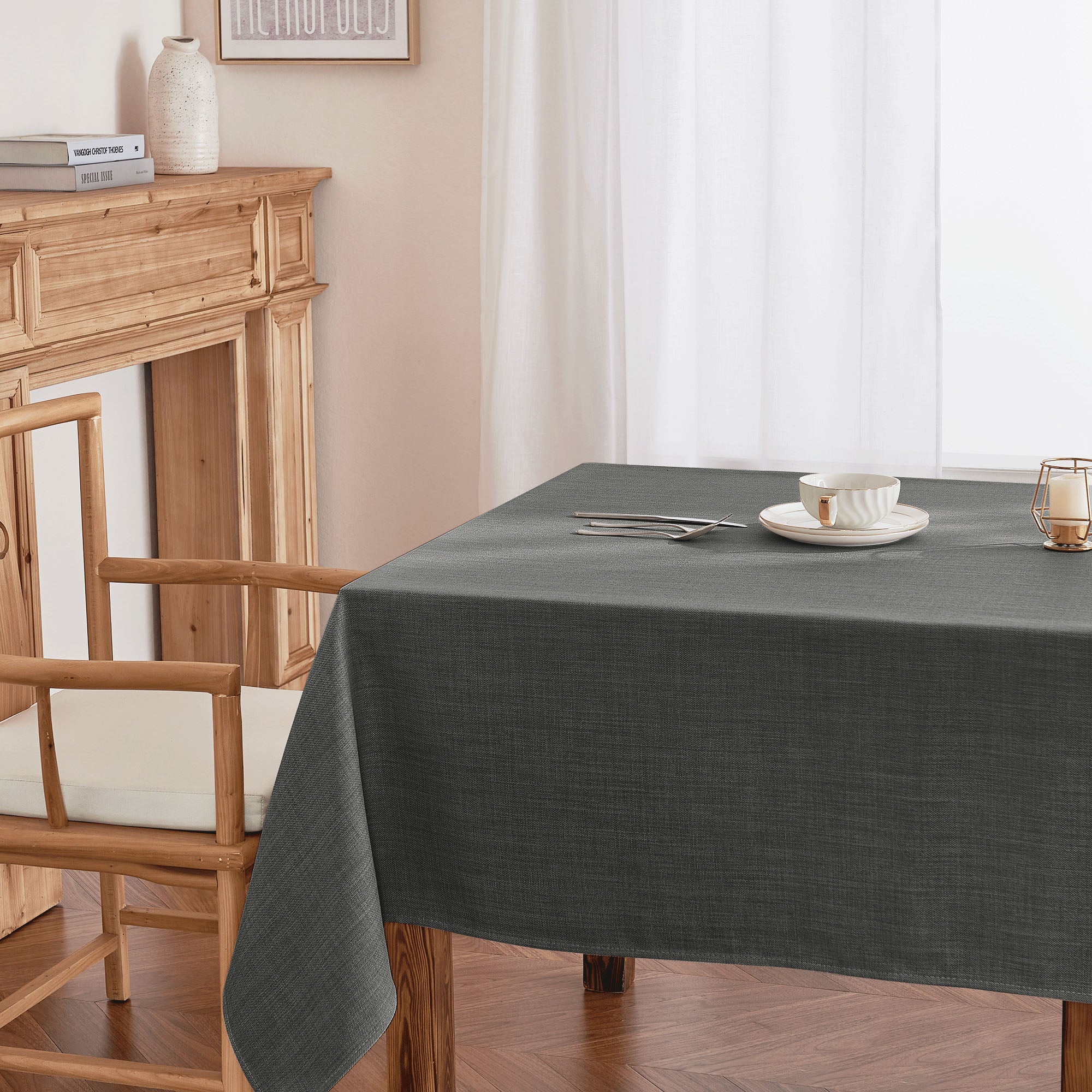 Dark gray linen-look tablecloth draped over a wooden dining table, with a white teacup and cutlery on top.