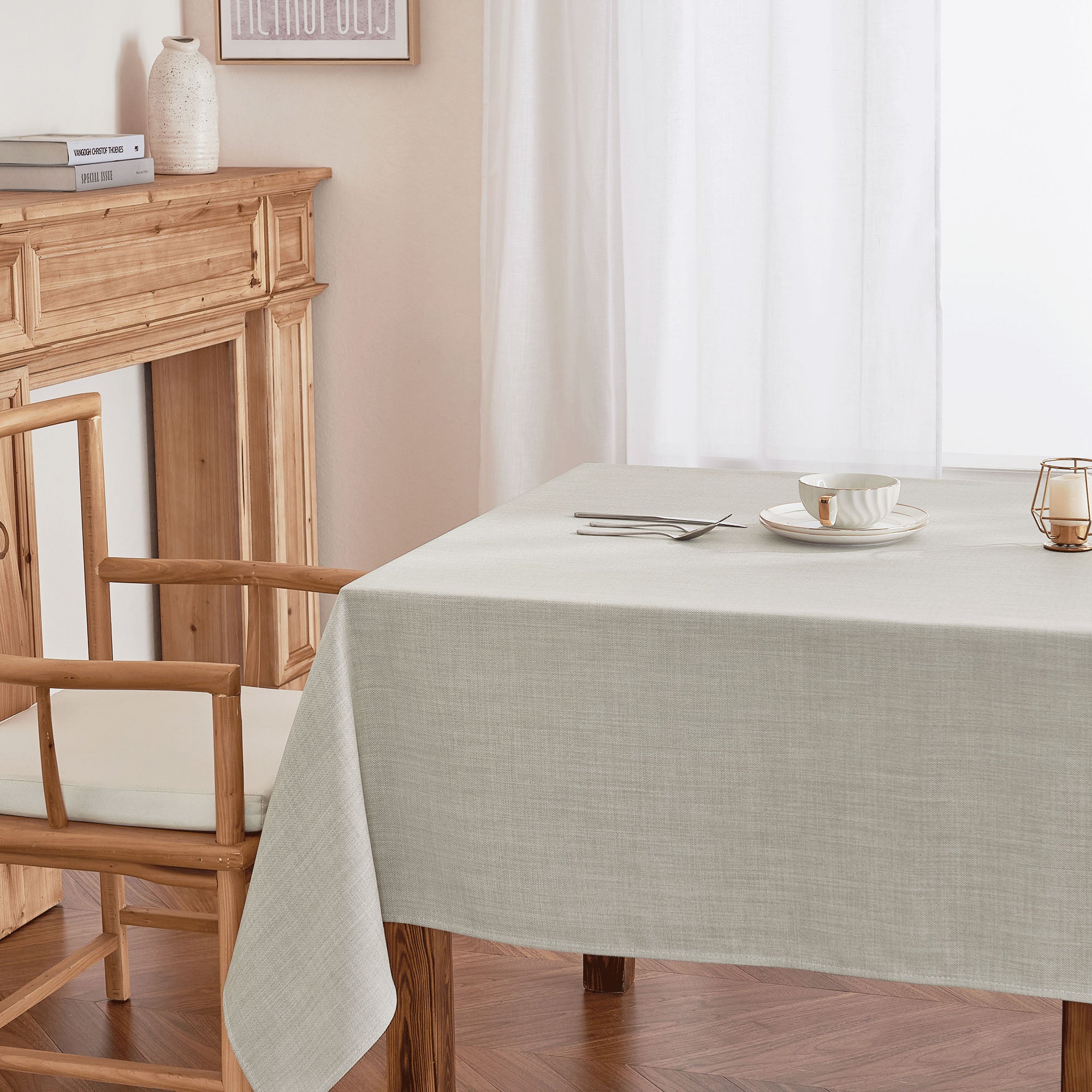Neutral light grey woven tablecloth draped over a wooden dining table, set with cutlery, bowl, and candle.