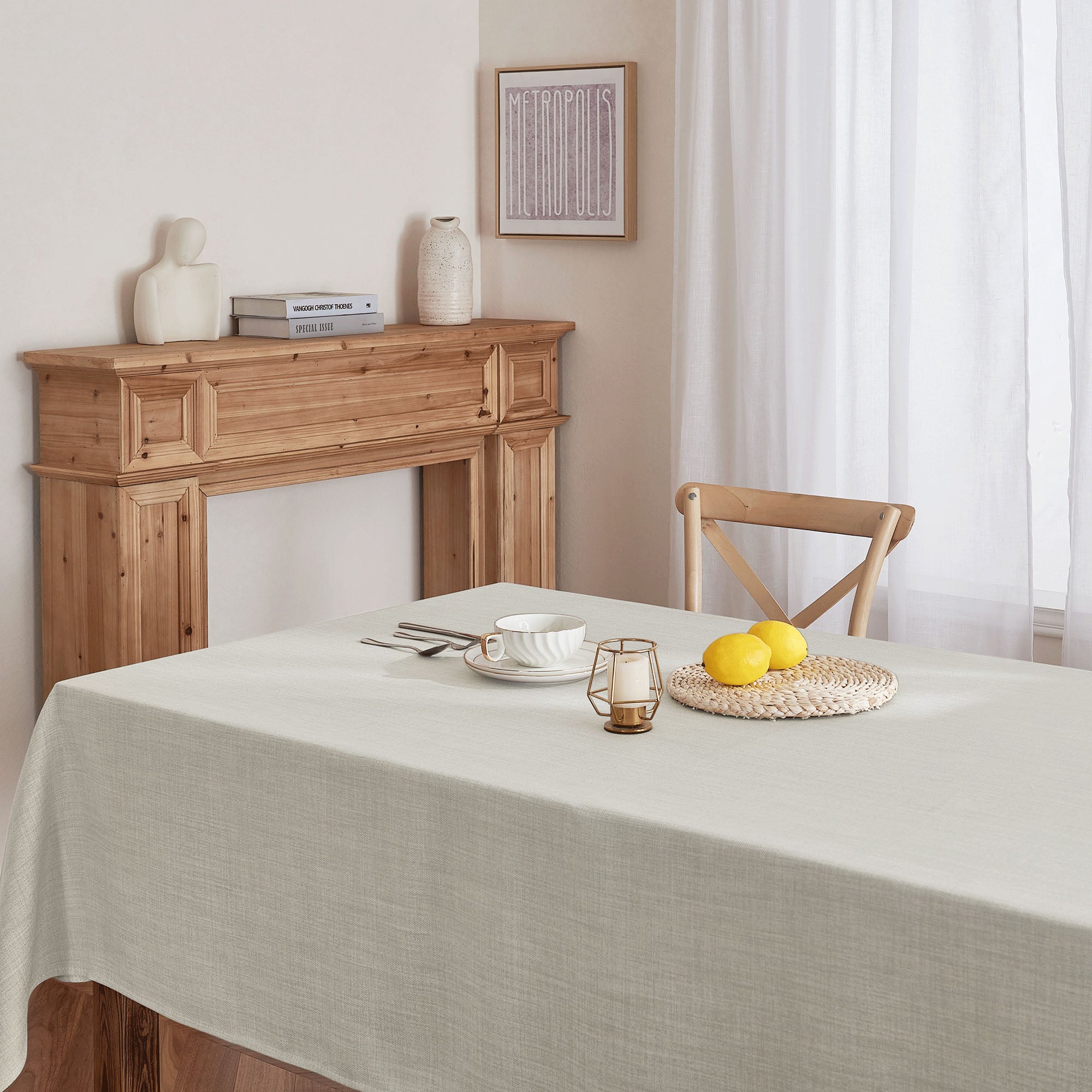 Light grey linen-look tablecloth covering a dining table, featuring a single place setting with a teacup, lemons, and a candle.