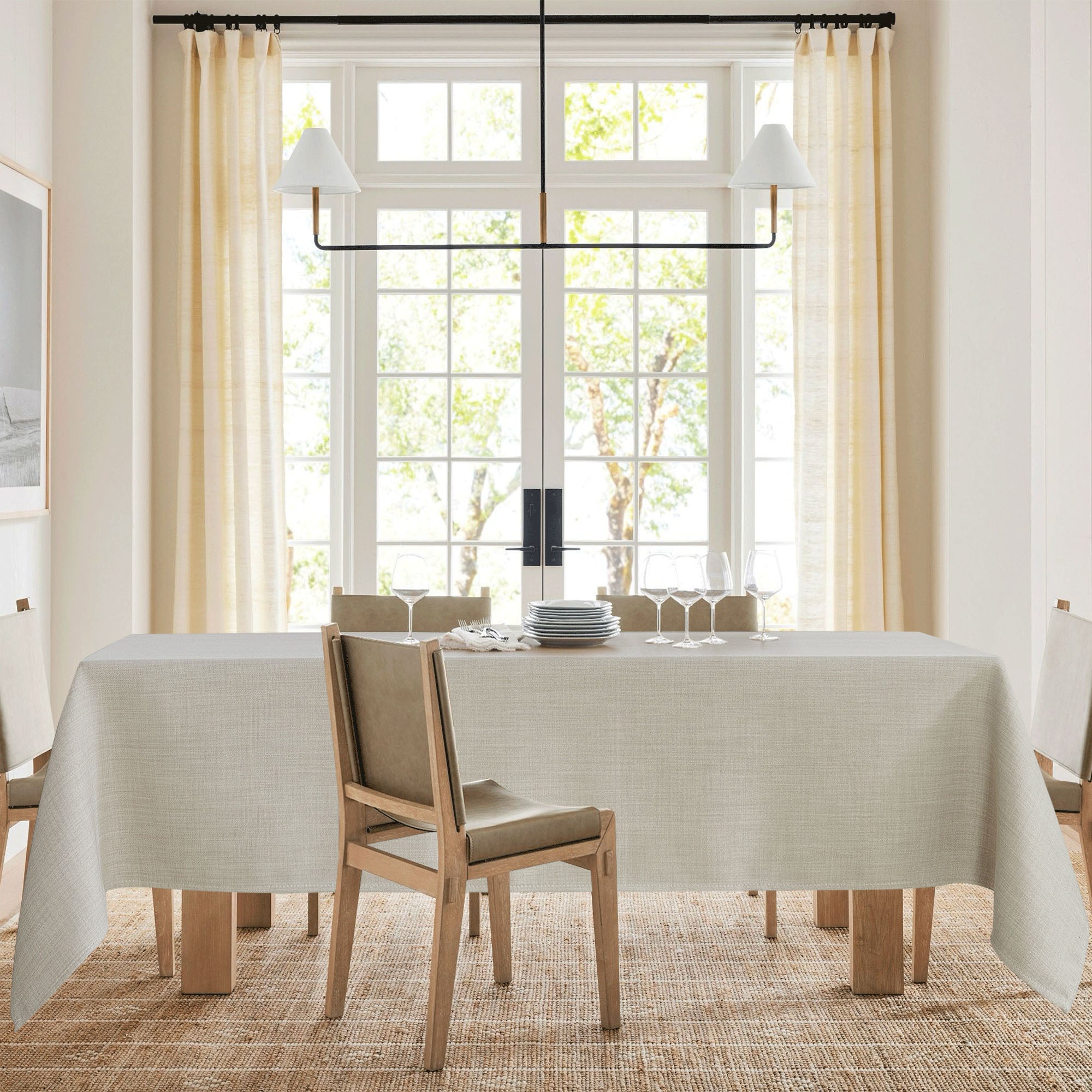 Light beige textured tablecloth on a dining table set with plates & wine glasses in a bright dining room.