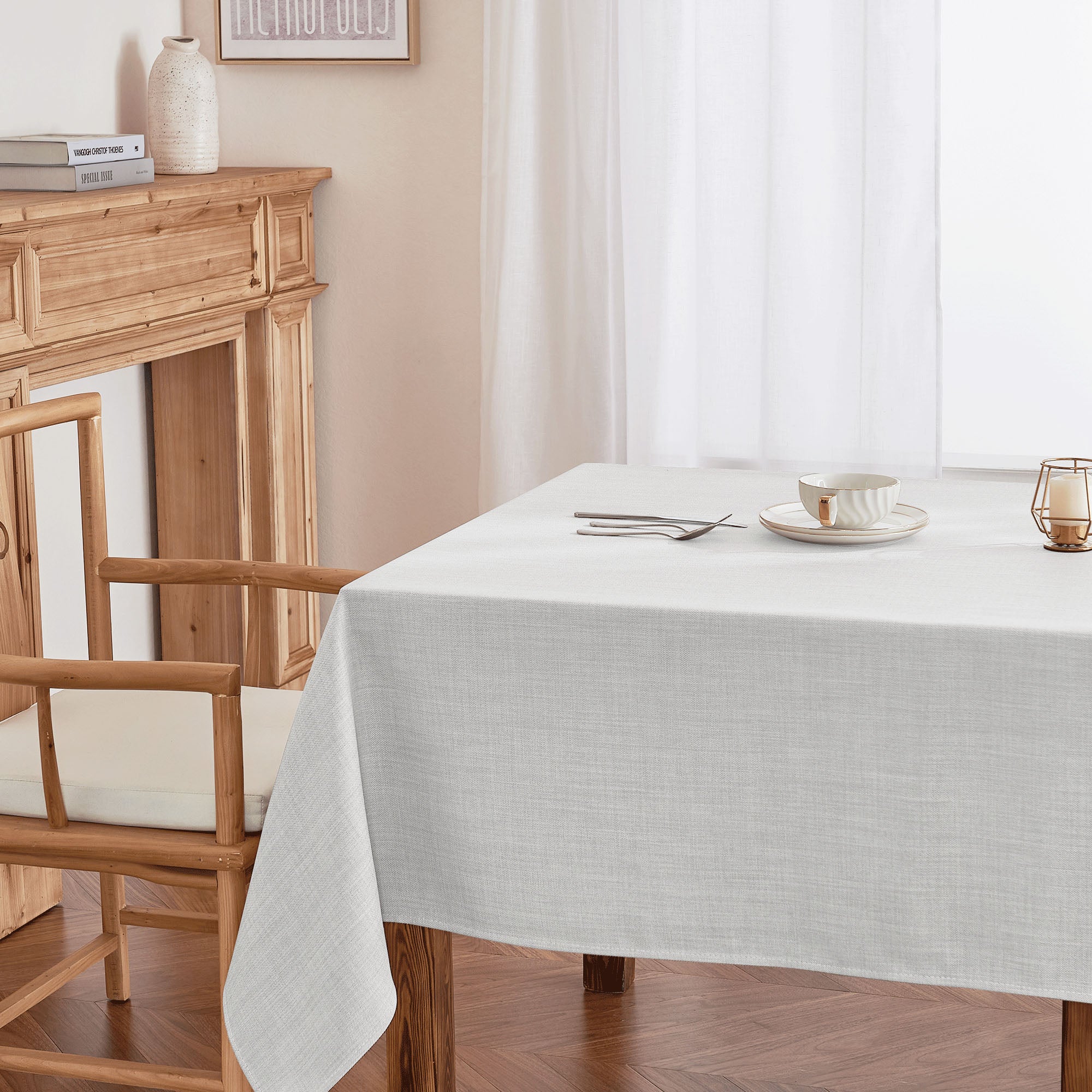 Light grey fabric tablecloth on a wooden dining table, showcasing its textured surface and elegant drape, set with a minimalist cup and cutlery.