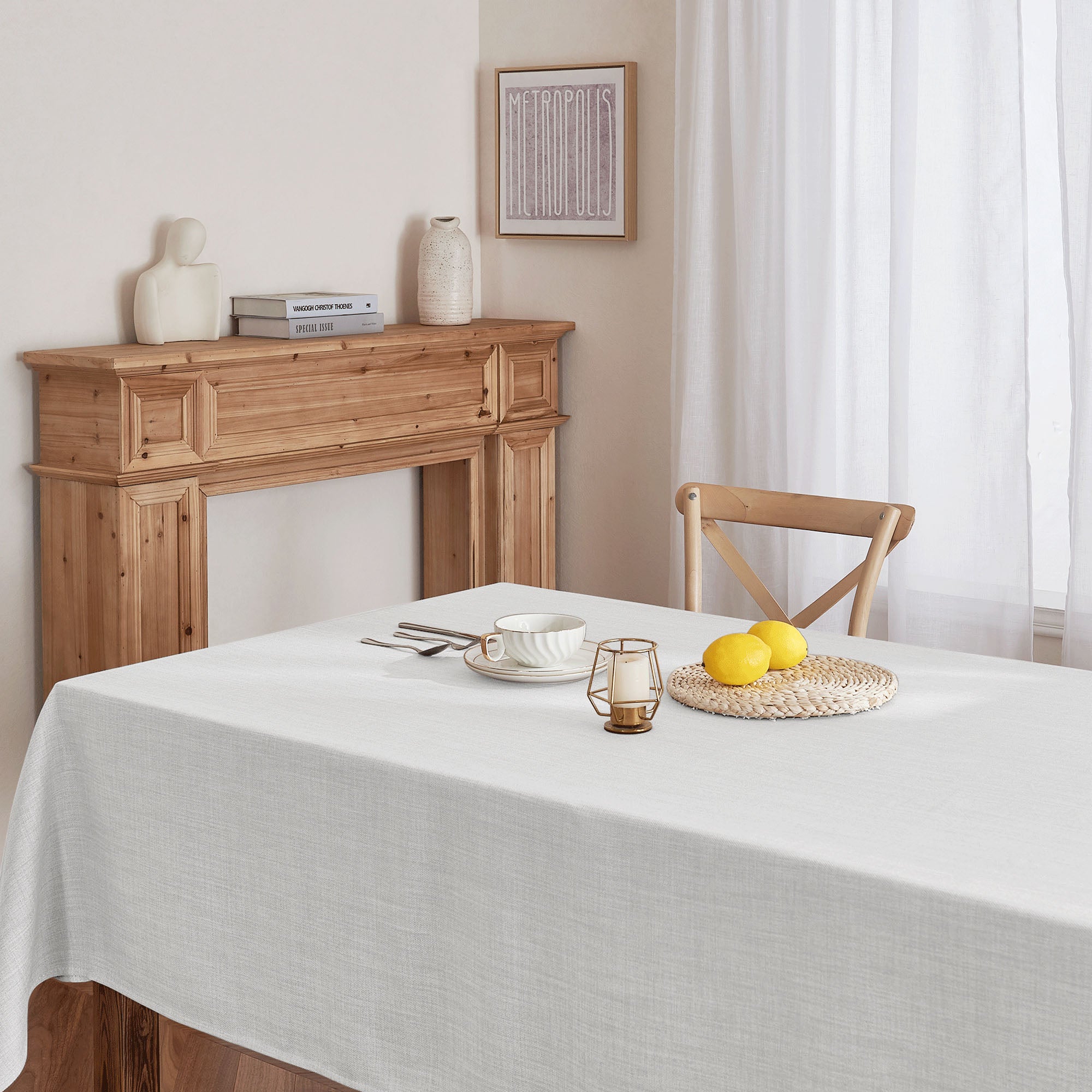 Light grey linen texture tablecloth on a dining table, styled with a teacup, cutlery, lemons, and a candle holder.