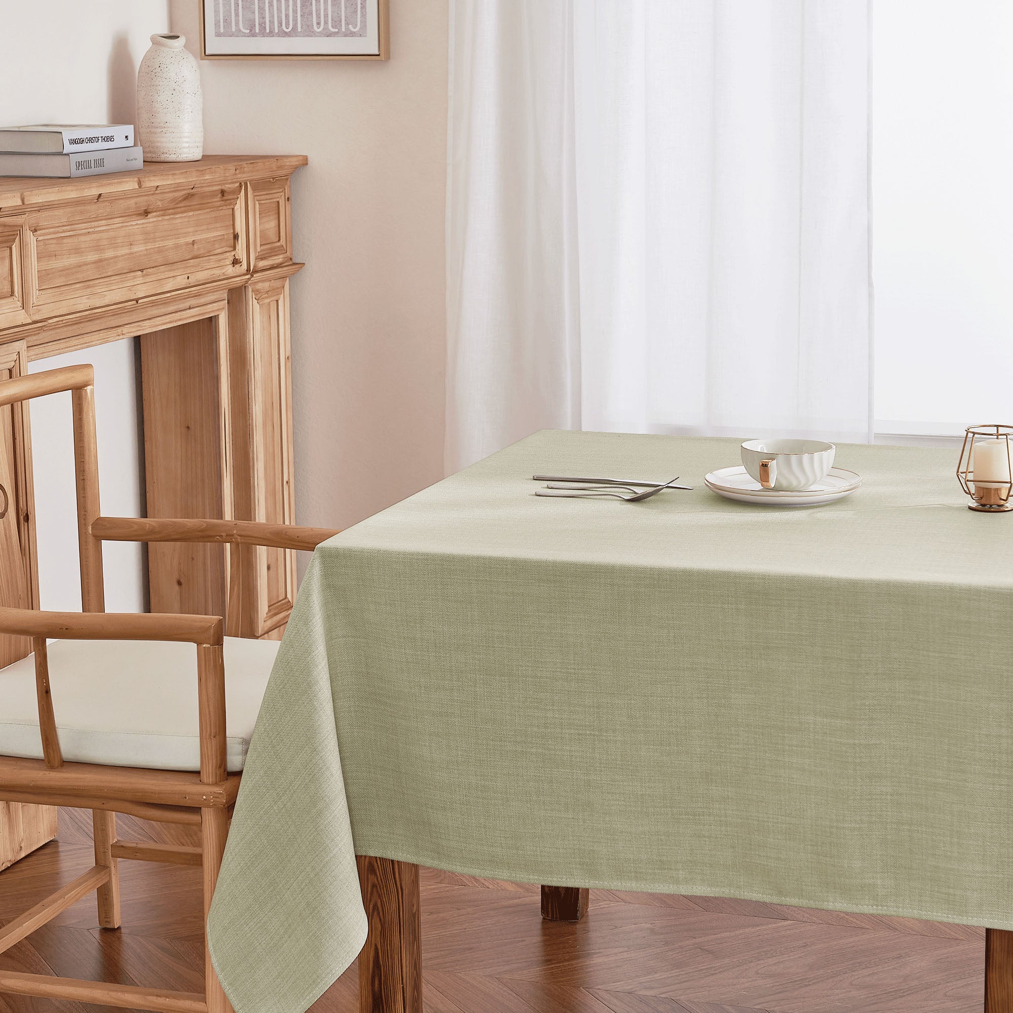 Sage green tablecloth with a subtle textured fabric on a wooden dining table, set with a bowl, plate, and cutlery.
