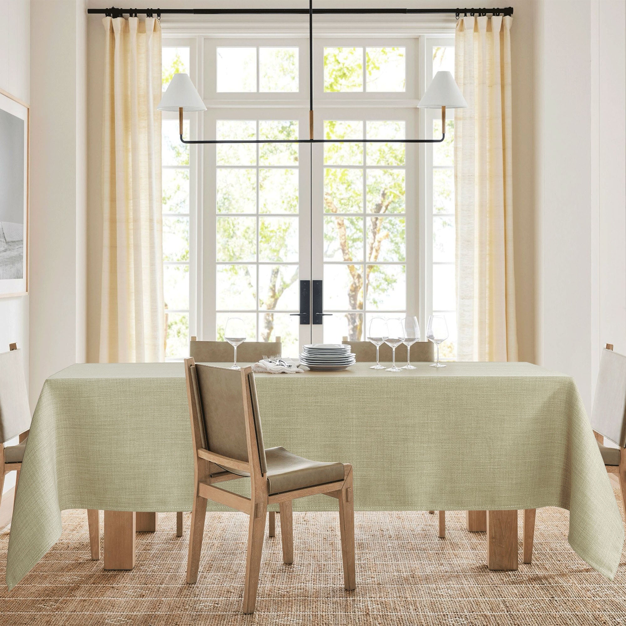 Light green textured tablecloth draped over a dining table set with white plates and wine glasses in a bright dining room.