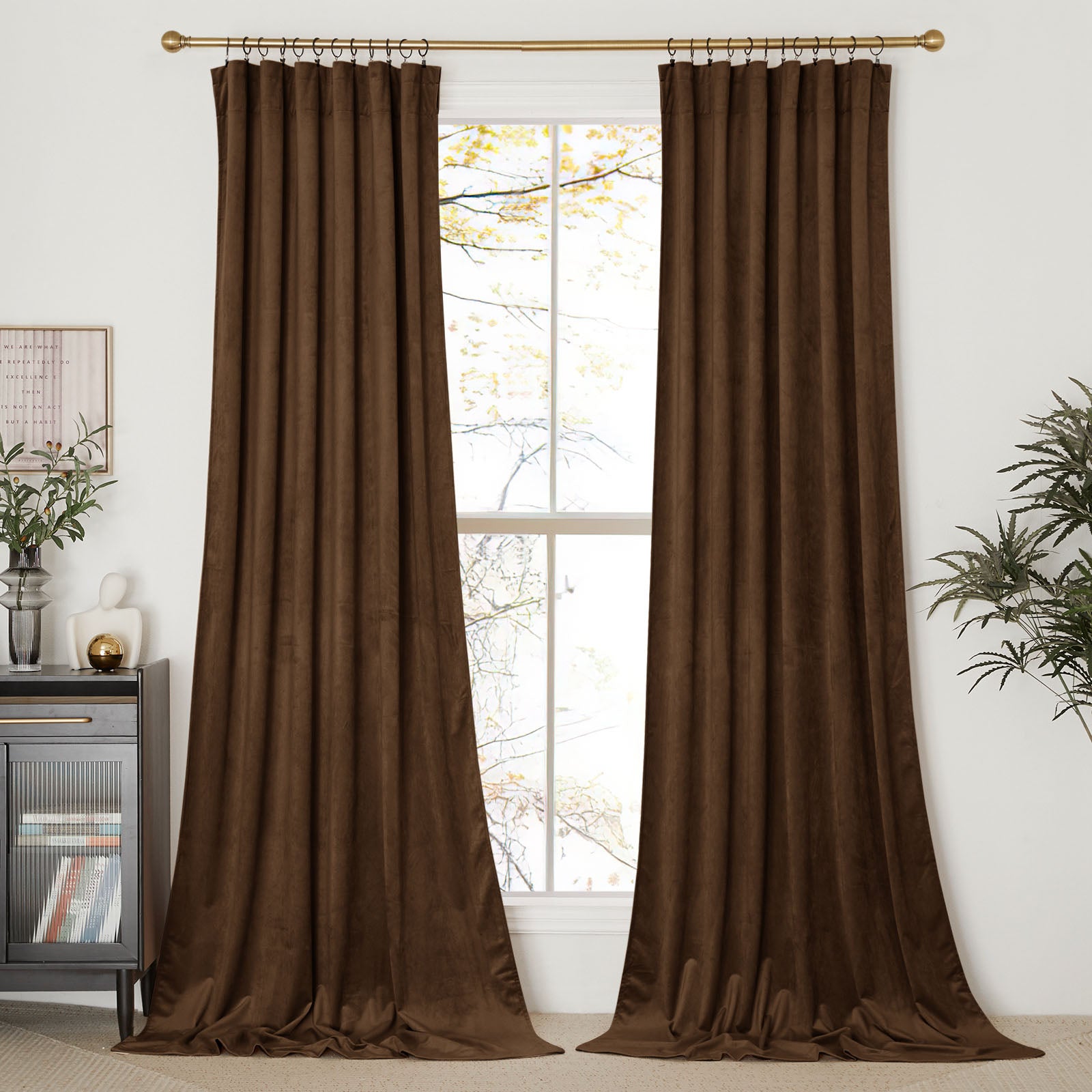 A pair of long, brown velvet curtains hanging on a brass rod, framing a tall window in a bright, modern room.