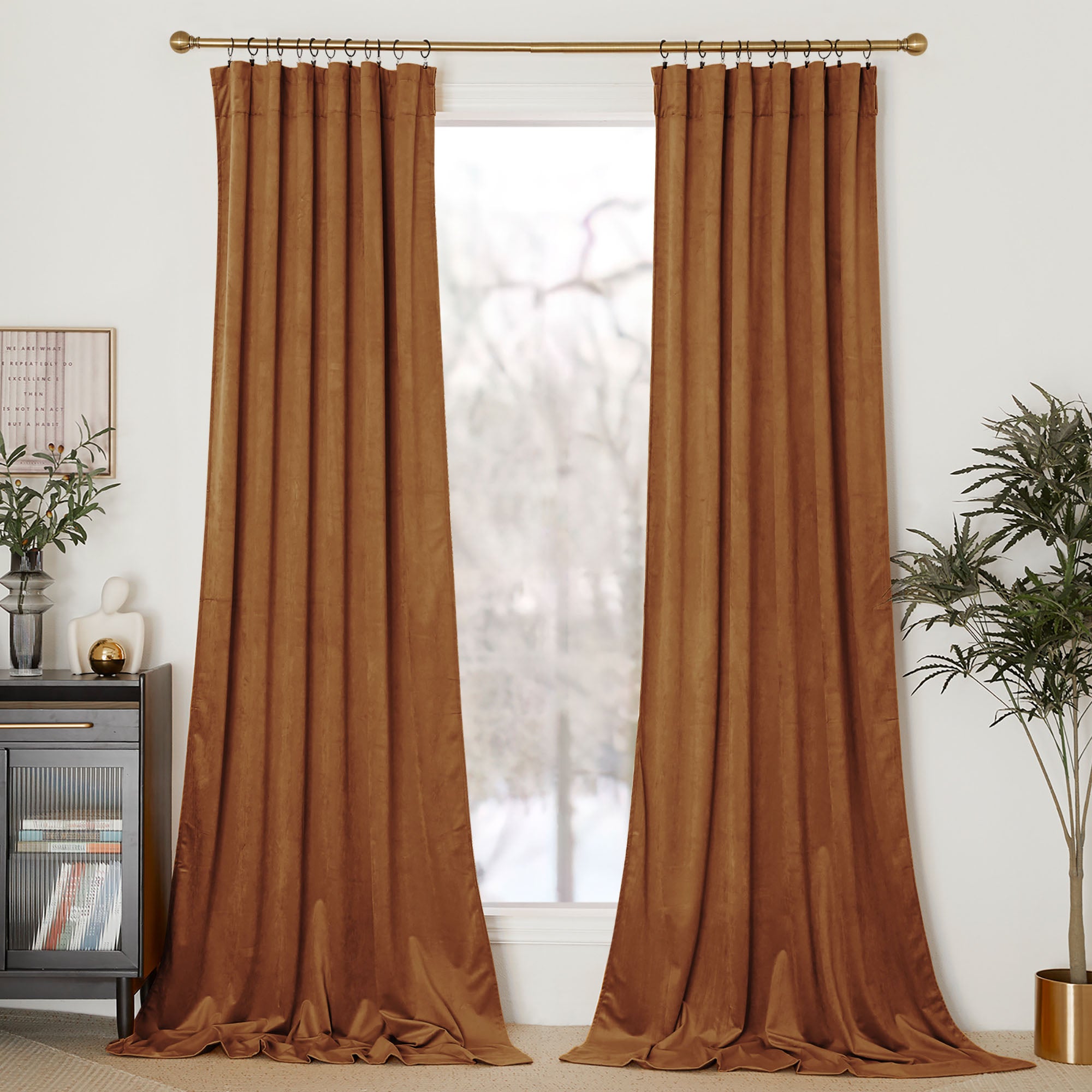 A pair of floor-length rust velvet curtains hang on a gold rod, framing a window in a modern living room.