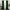 A pair of floor-length dark green velvet curtains hanging on a gold curtain rod with rings, framing a window.
