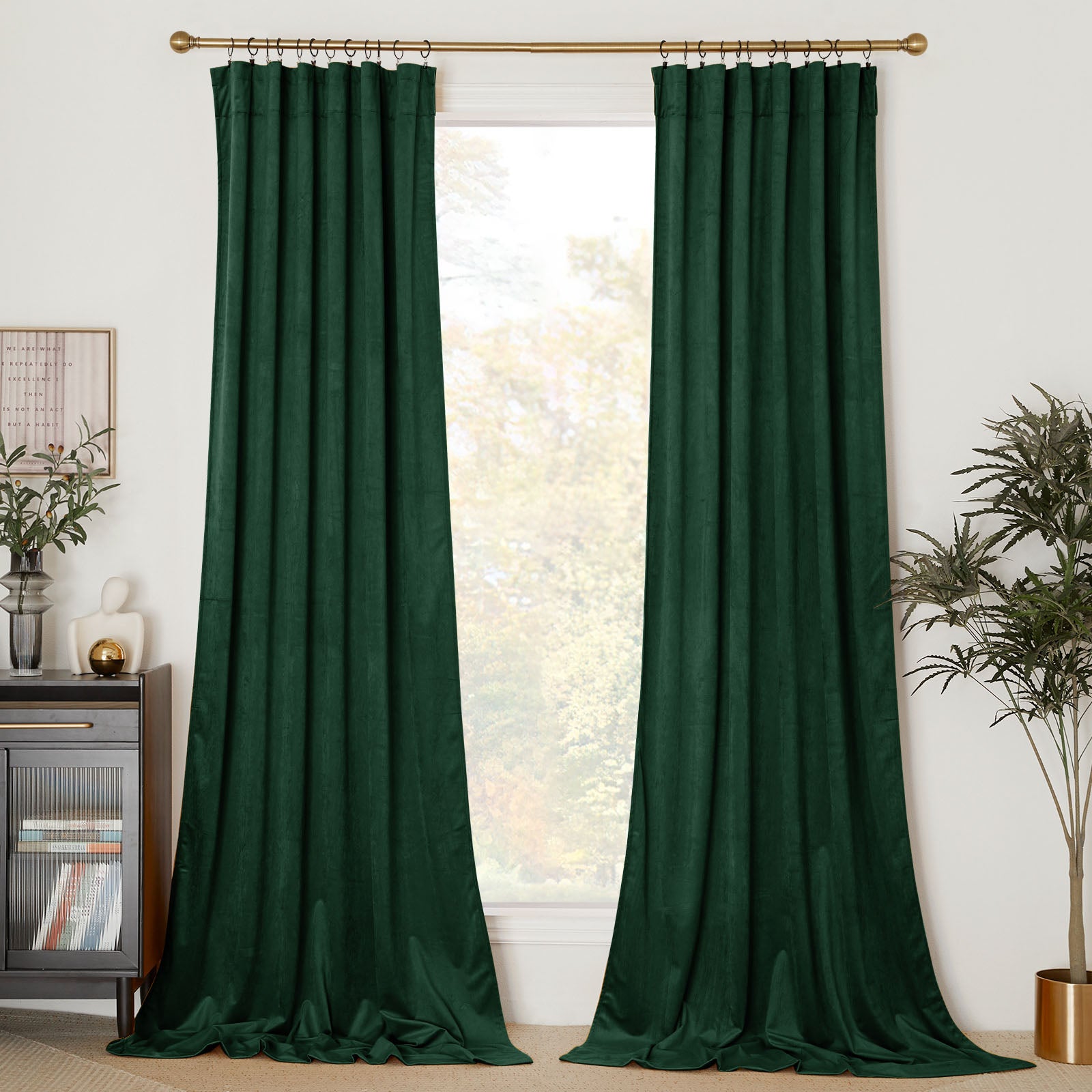 A pair of floor-length dark green velvet curtains hanging on a gold curtain rod with rings, framing a window.