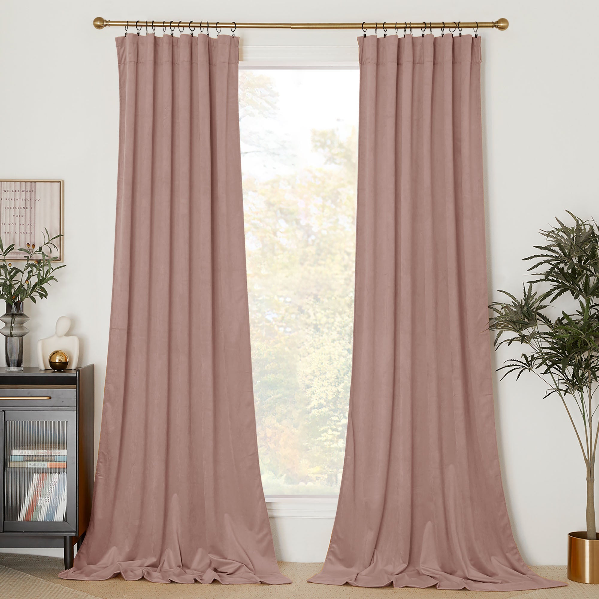 Dusty rose velvet curtains hanging on a gold rod with clip rings, framing a window in a styled living room.