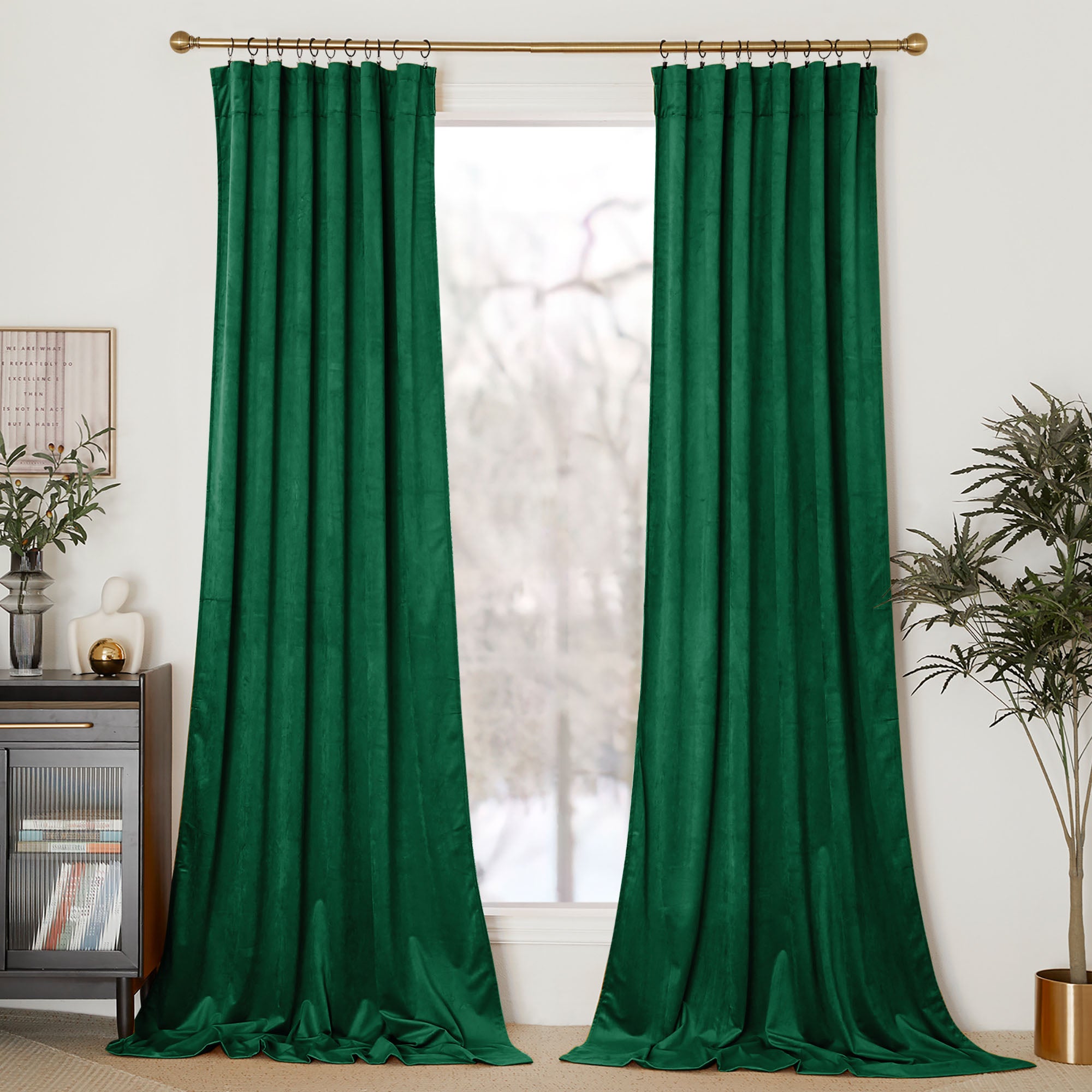 Two emerald green velvet curtains hanging on a gold rod in a modern living room, pooling elegantly on the floor.