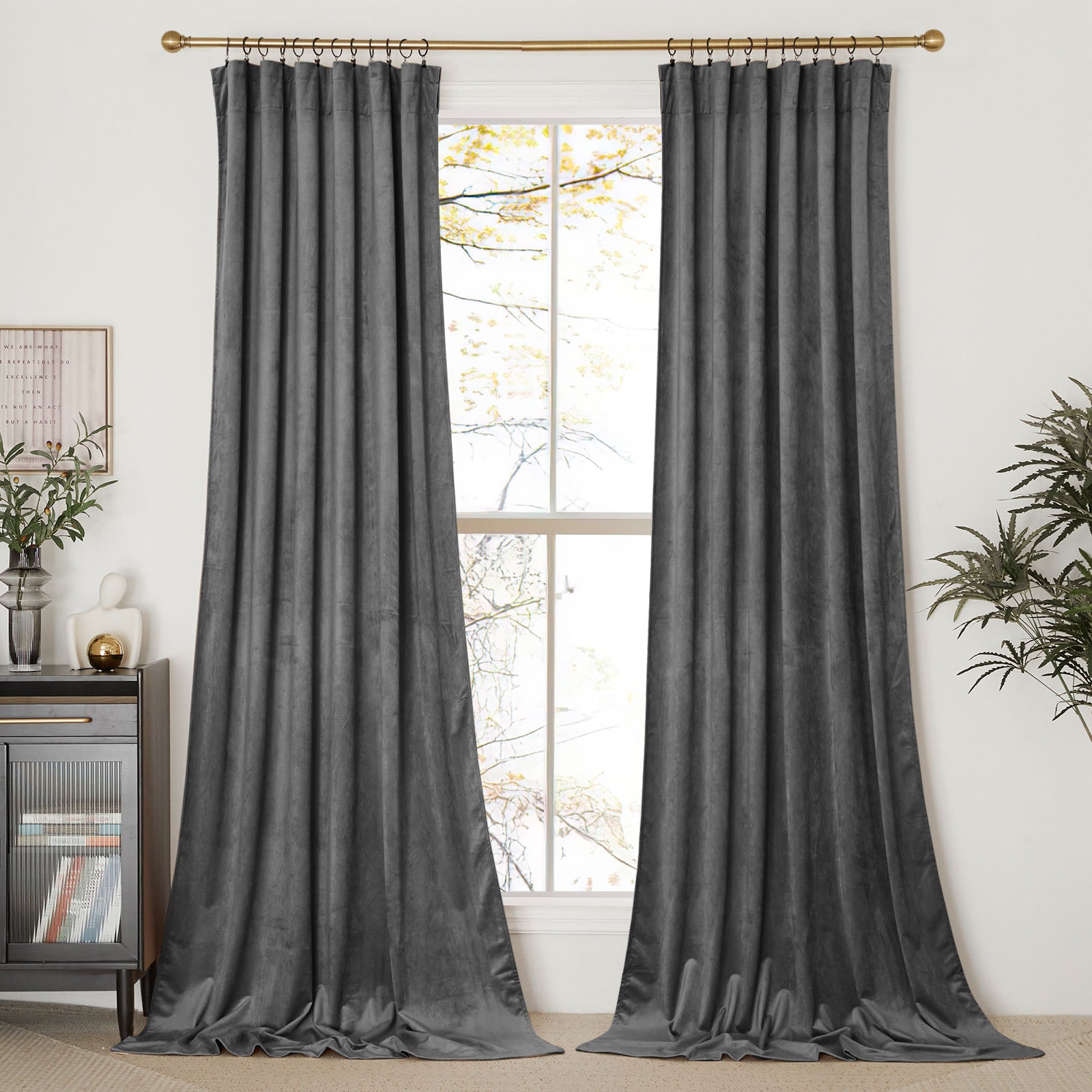 A pair of floor-length, pleated dark grey velvet curtains hung with rings on a brass rod in a living room.