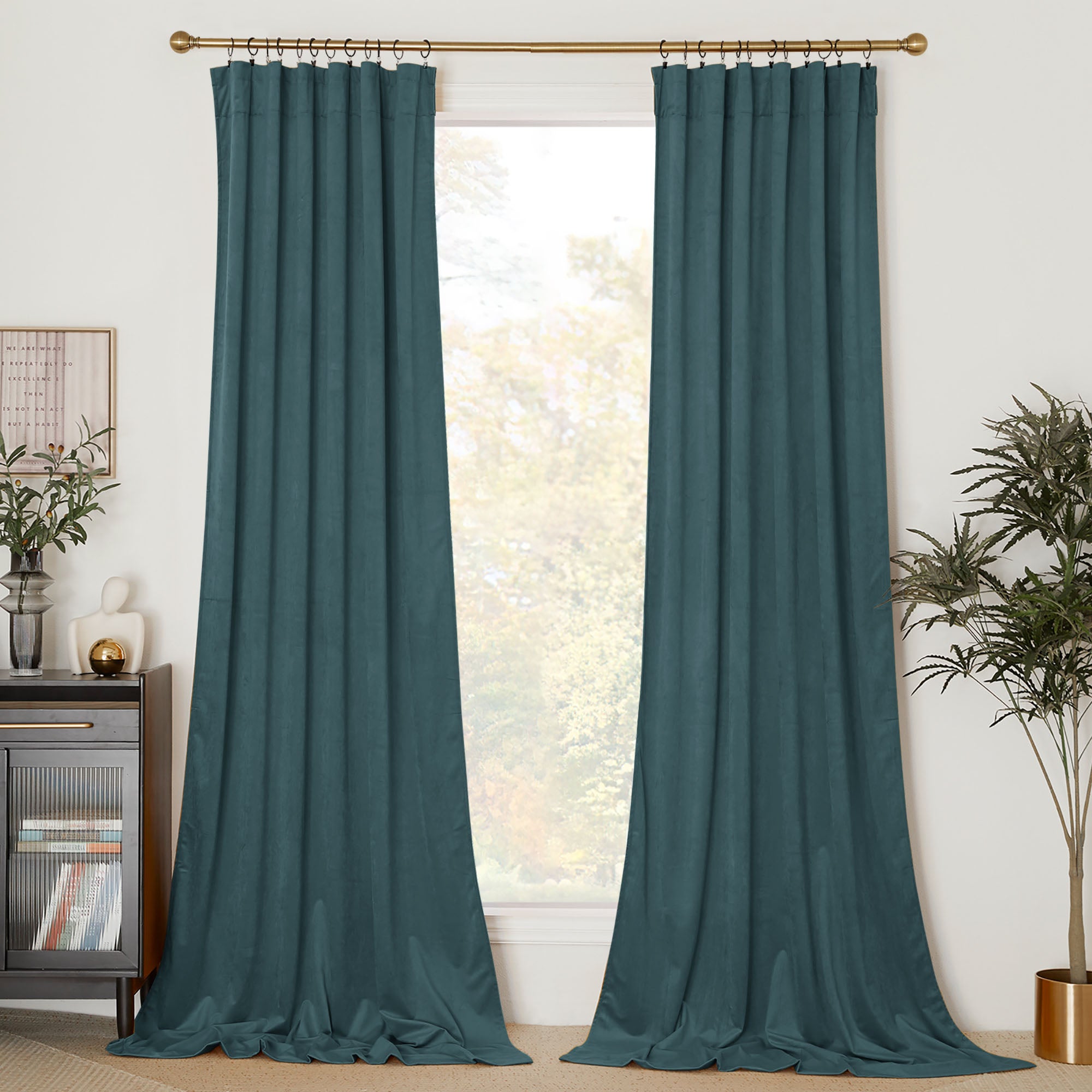 A pair of long teal velvet curtains hanging from a gold rod with rings, framing a window in a contemporary living room.