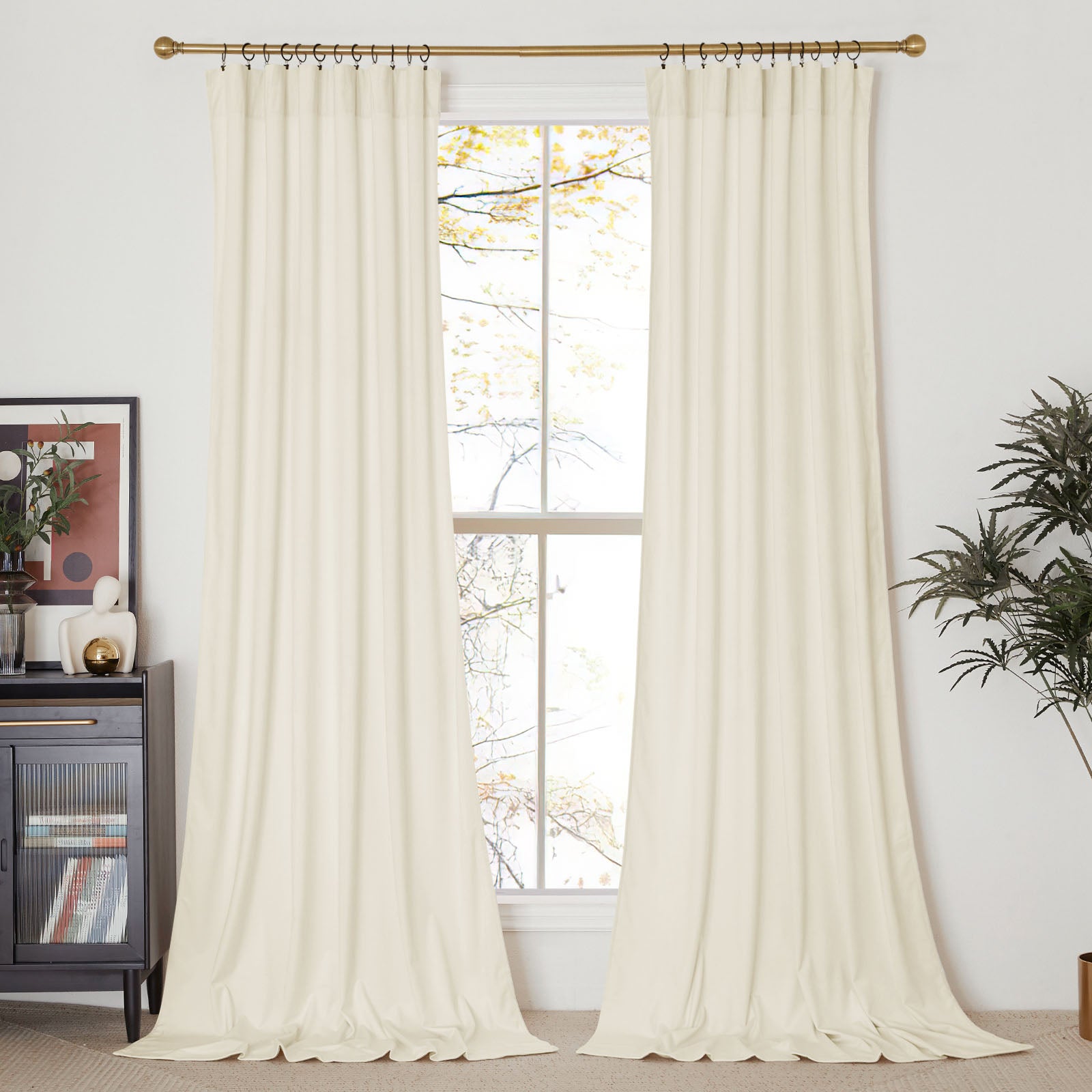 Long cream velvet curtains hanging on a gold rod with rings, framing a window in a fully decorated living room setting.