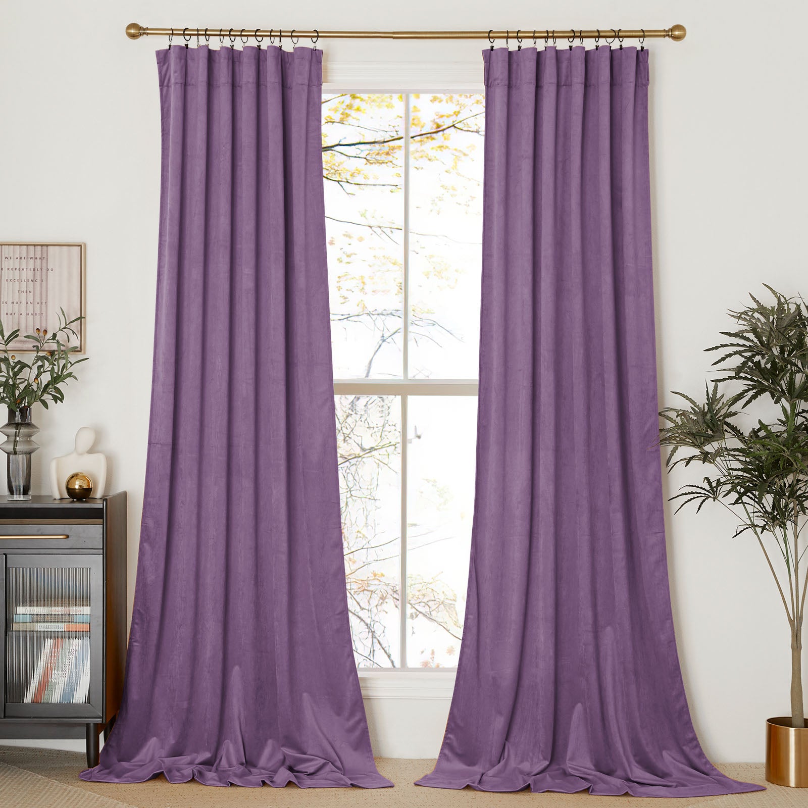 A pair of long, purple velvet curtains hanging on a gold rod, framing a tall window in a styled living room.