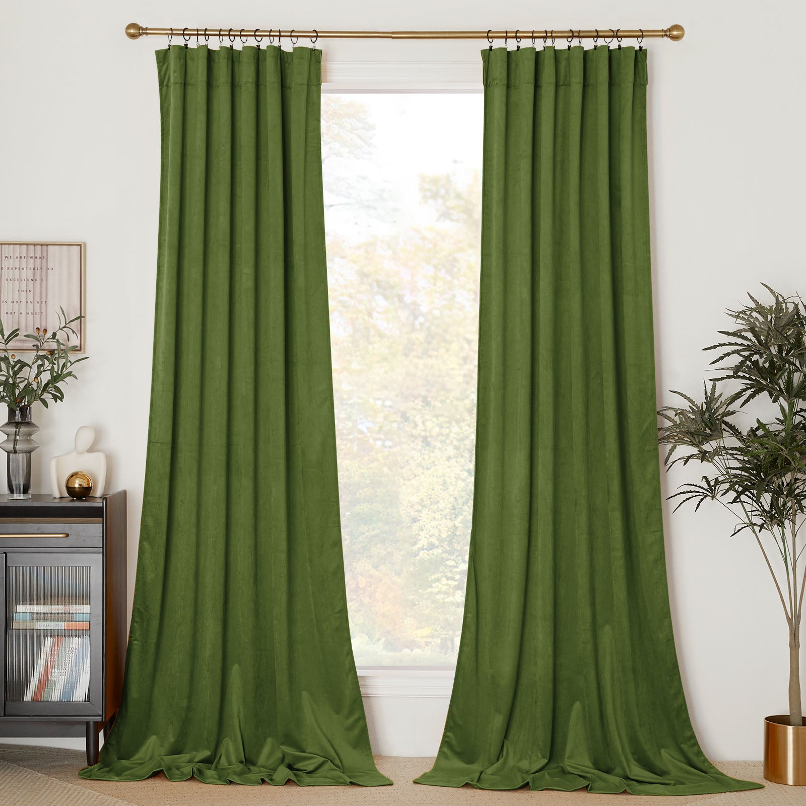 A pair of long, olive green velvet curtains hanging on a gold rod, framing a bright window in a decorated living room.