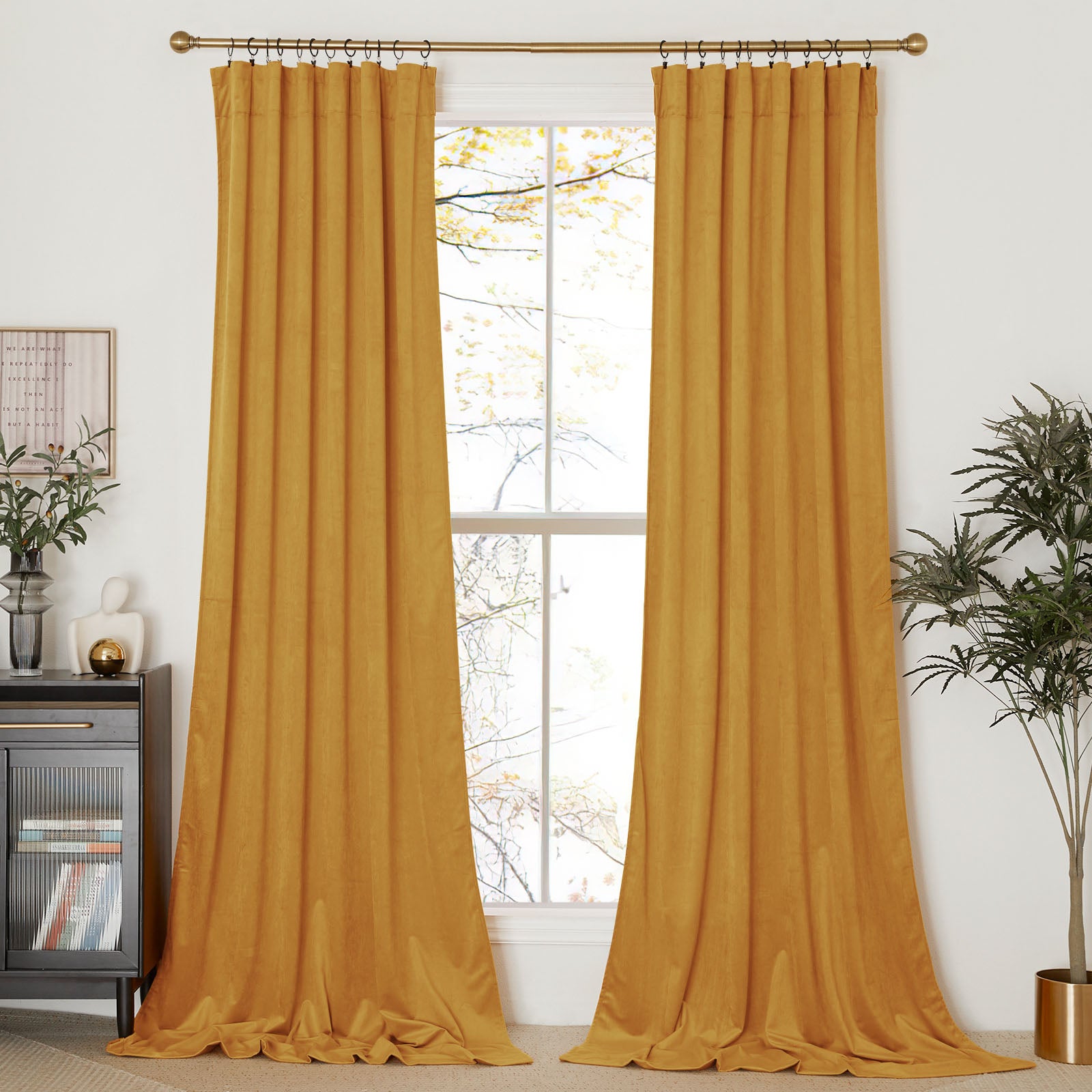 A pair of long mustard yellow velvet curtains hanging from a gold rod, framing a tall window in a brightly lit room.