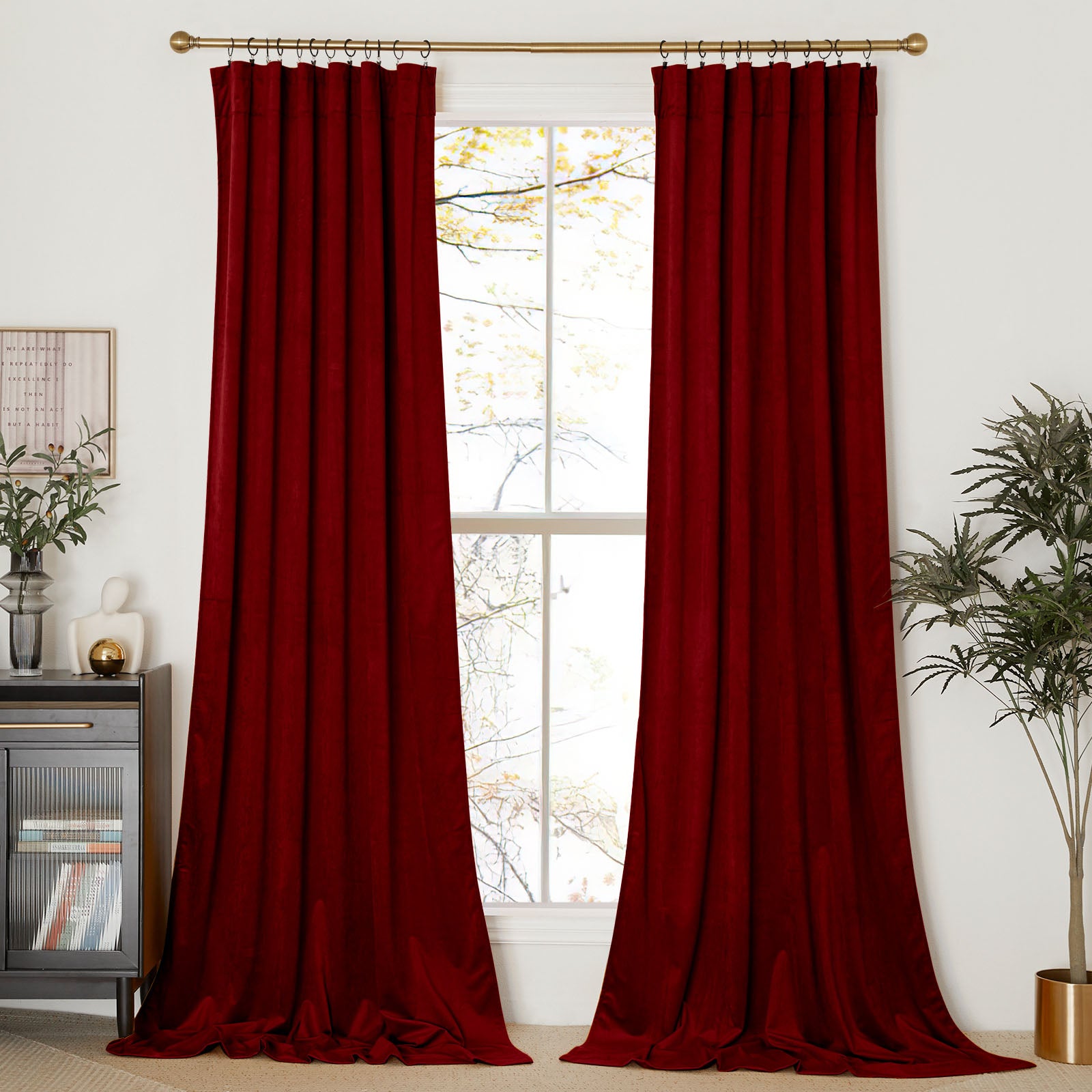 Full view of two rich red velvet curtains hanging from a gold rod, puddled on the floor and framing a tall window.