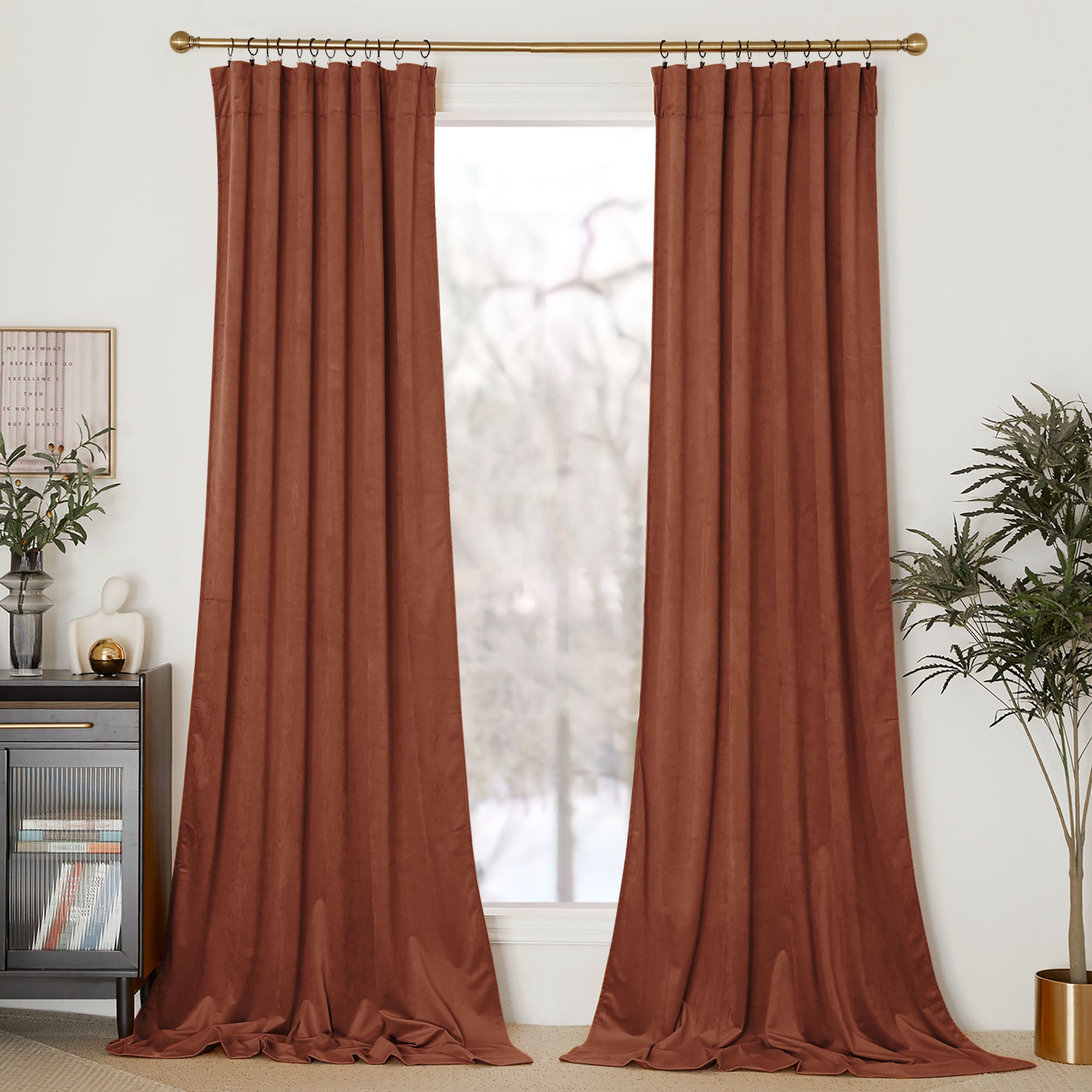 A pair of rust-colored velvet curtain panels hung on a gold rod with rings, shown fully closed in front of a window.