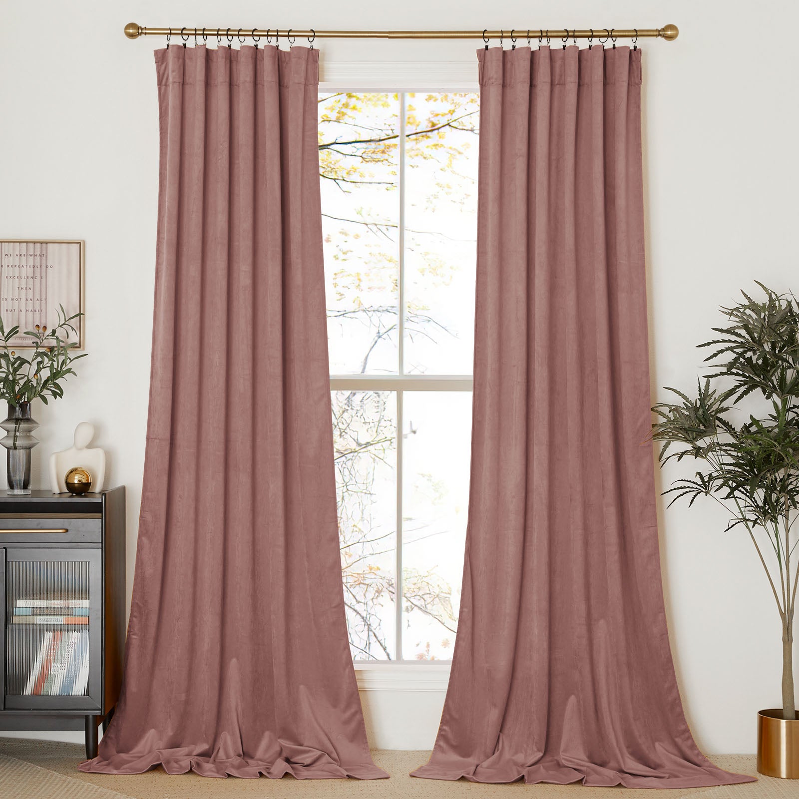 A pair of dusty rose velvet curtains hang on a gold rod with rings, framing a window in a contemporary living room.