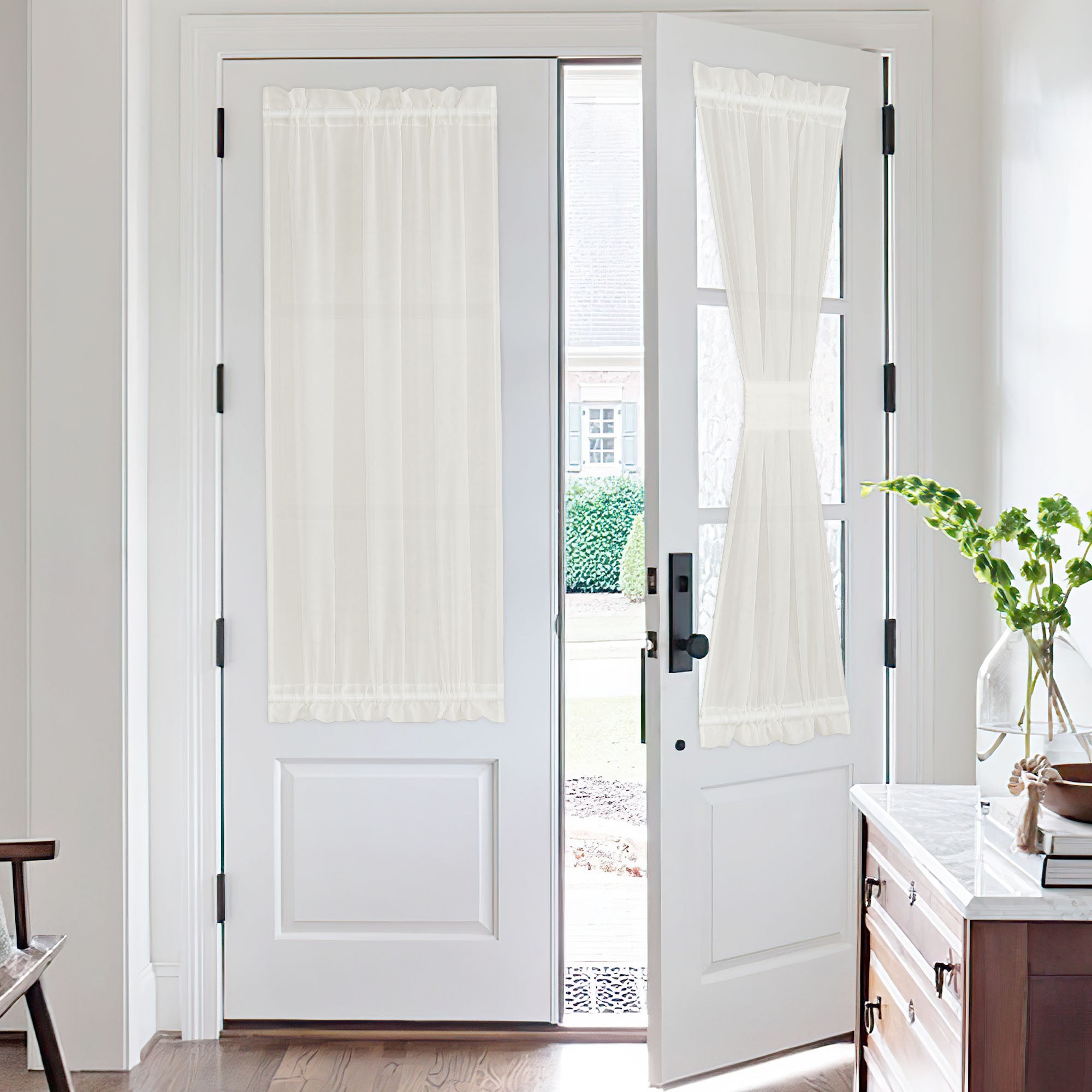 Two white French doors with sheer voile door curtains. One curtain hangs flat, while the other is tied back for an open look.