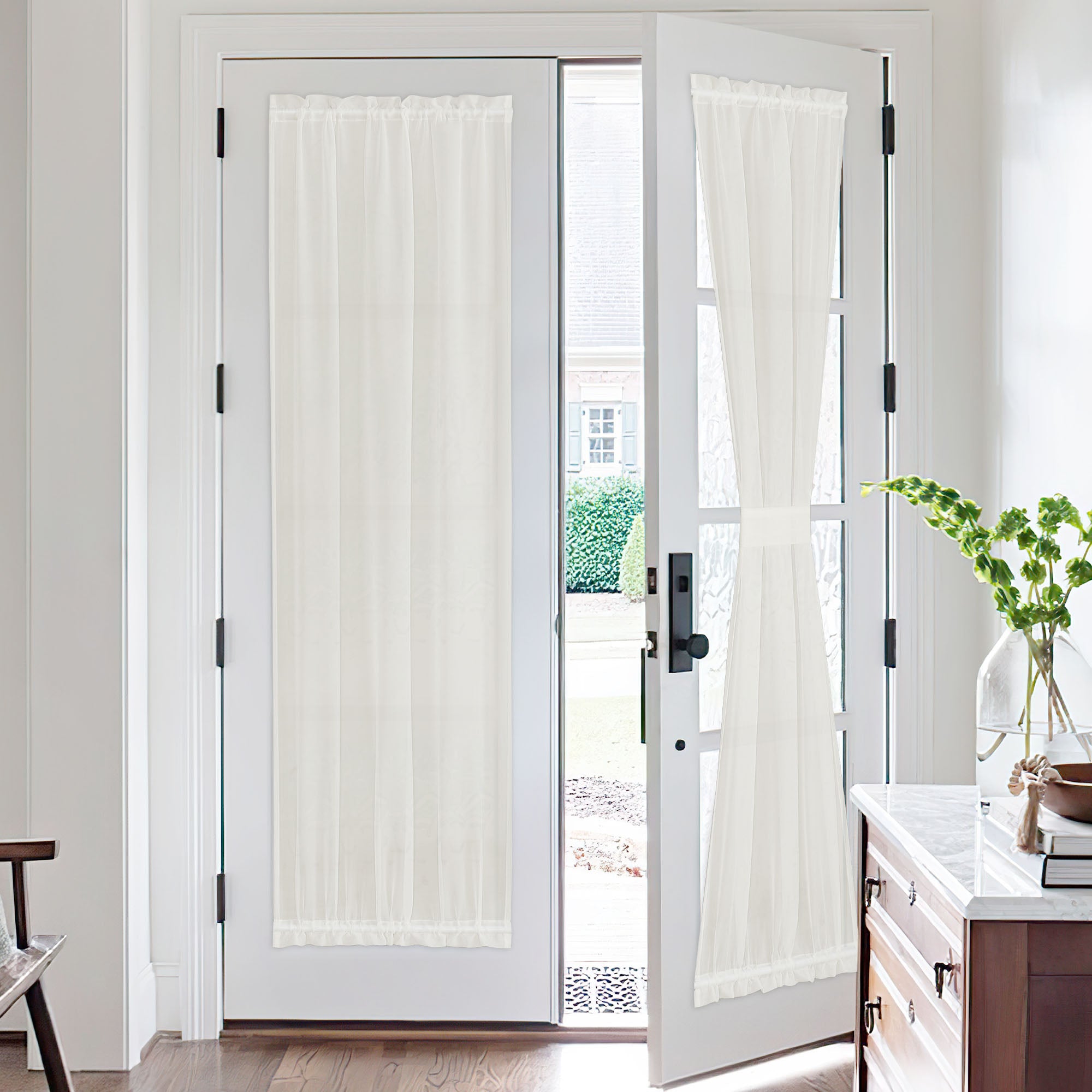 Light-colored voile sheer curtains on white French doors. One curtain is tied back, highlighting privacy and light filtering.