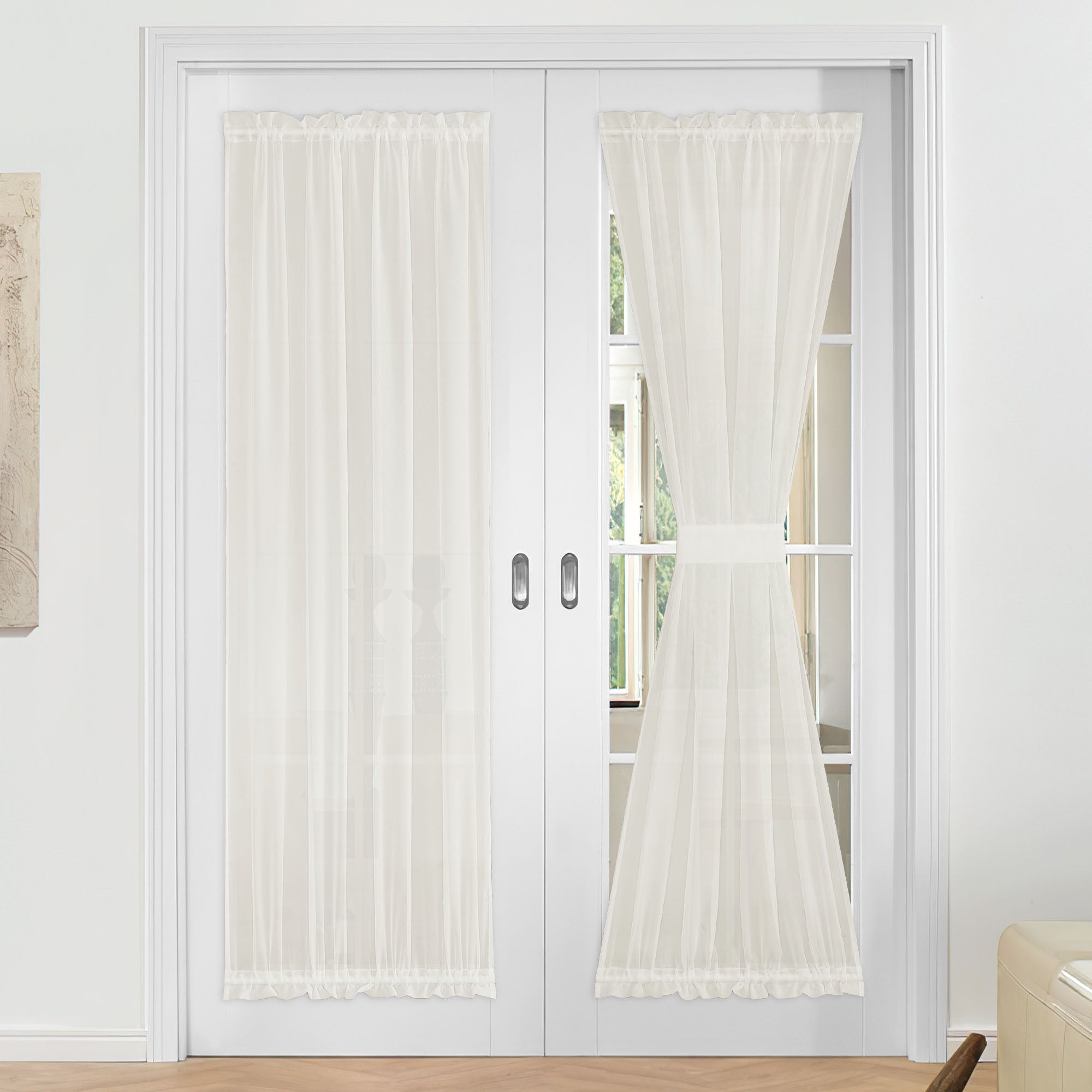 White voile sheer door curtains on French doors. One curtain hangs flat; the other is tied back with a matching fabric strap.