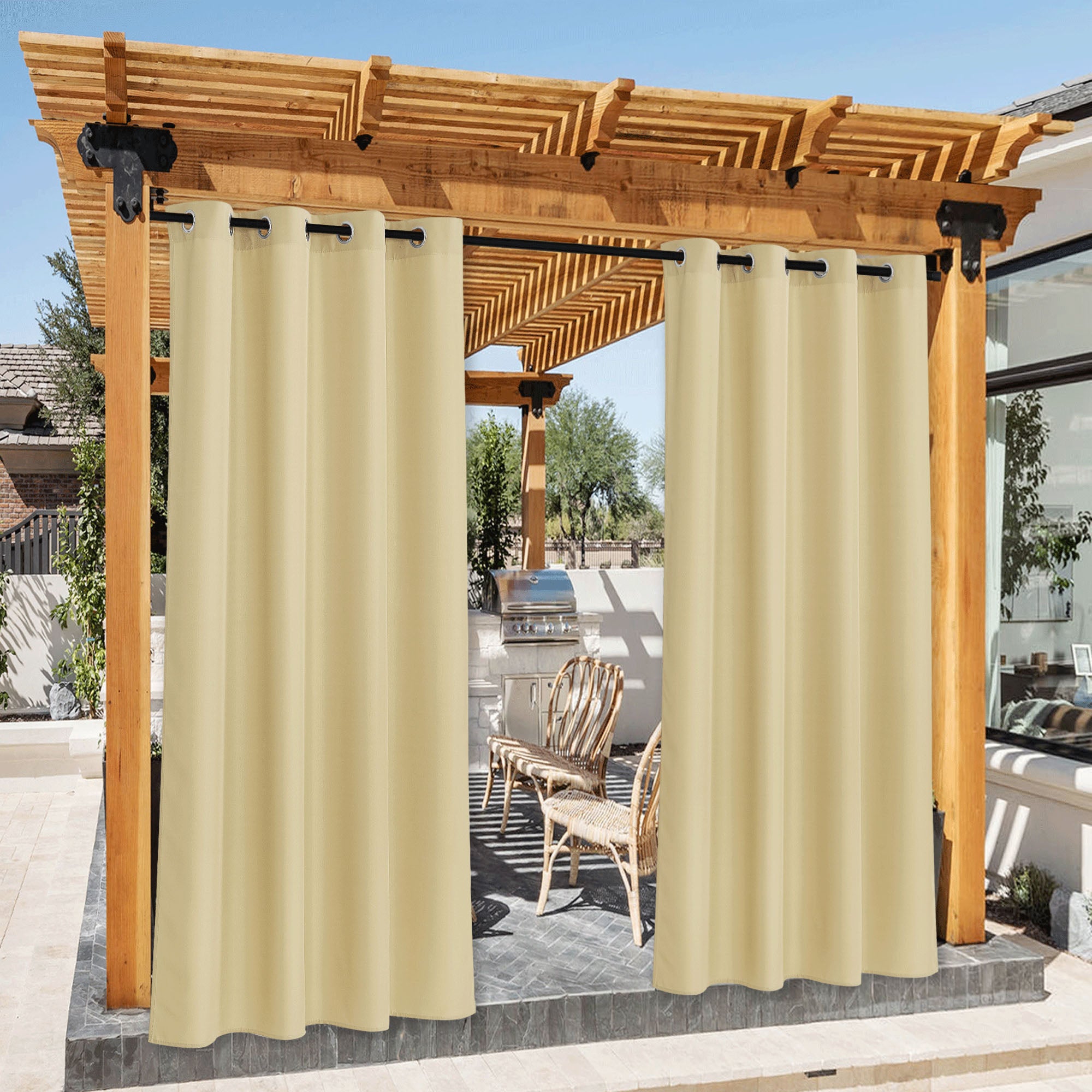 Cream waterproof canvas outdoor curtains on a pergola, providing privacy & shade for a sunny patio with an outdoor kitchen.