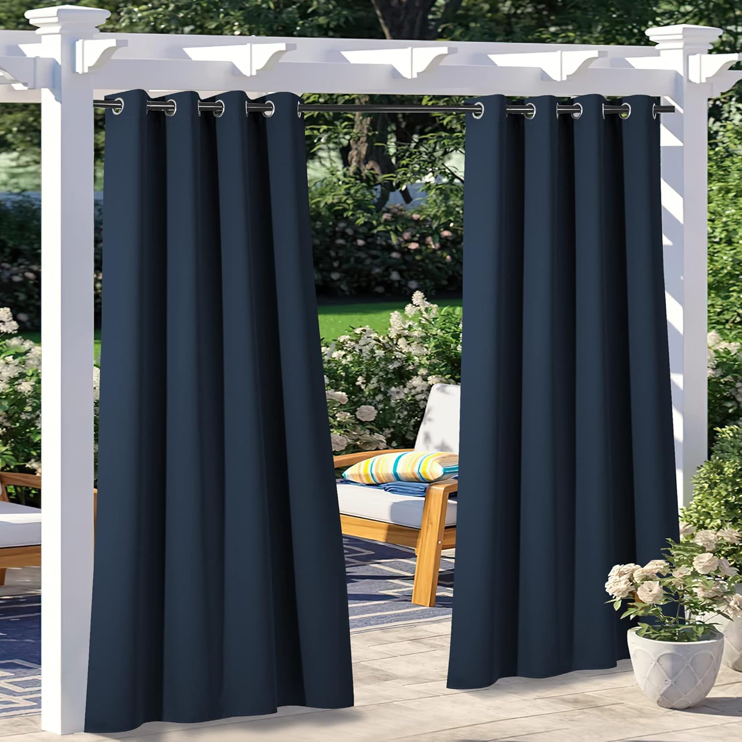 Two navy blue custom outdoor curtains with grommets, hanging on a white pergola. Partial view of an outdoor patio and garden.