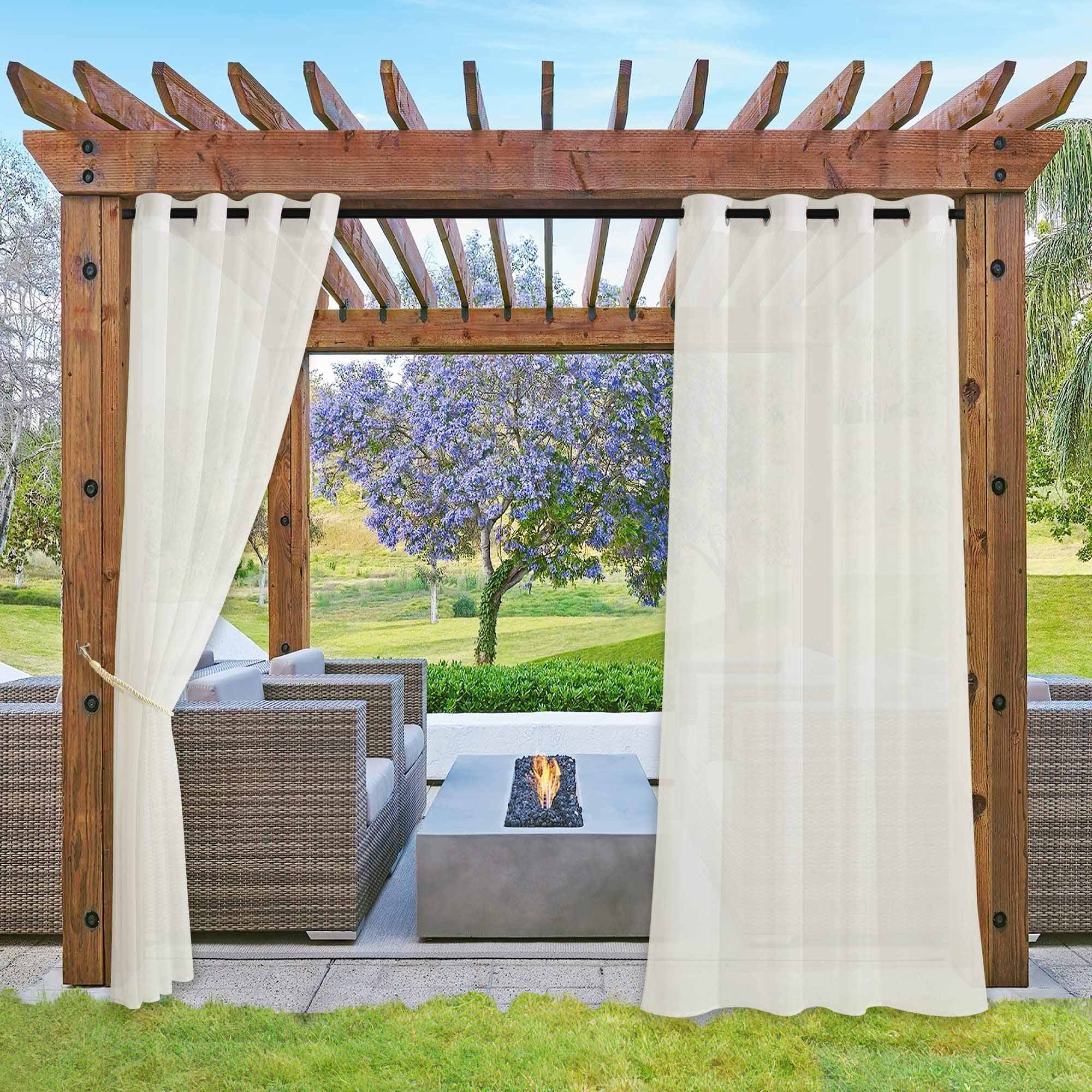 Waterproof sheer white outdoor curtains on a wooden pergola, one tied back, framing an outdoor patio with a fire pit.