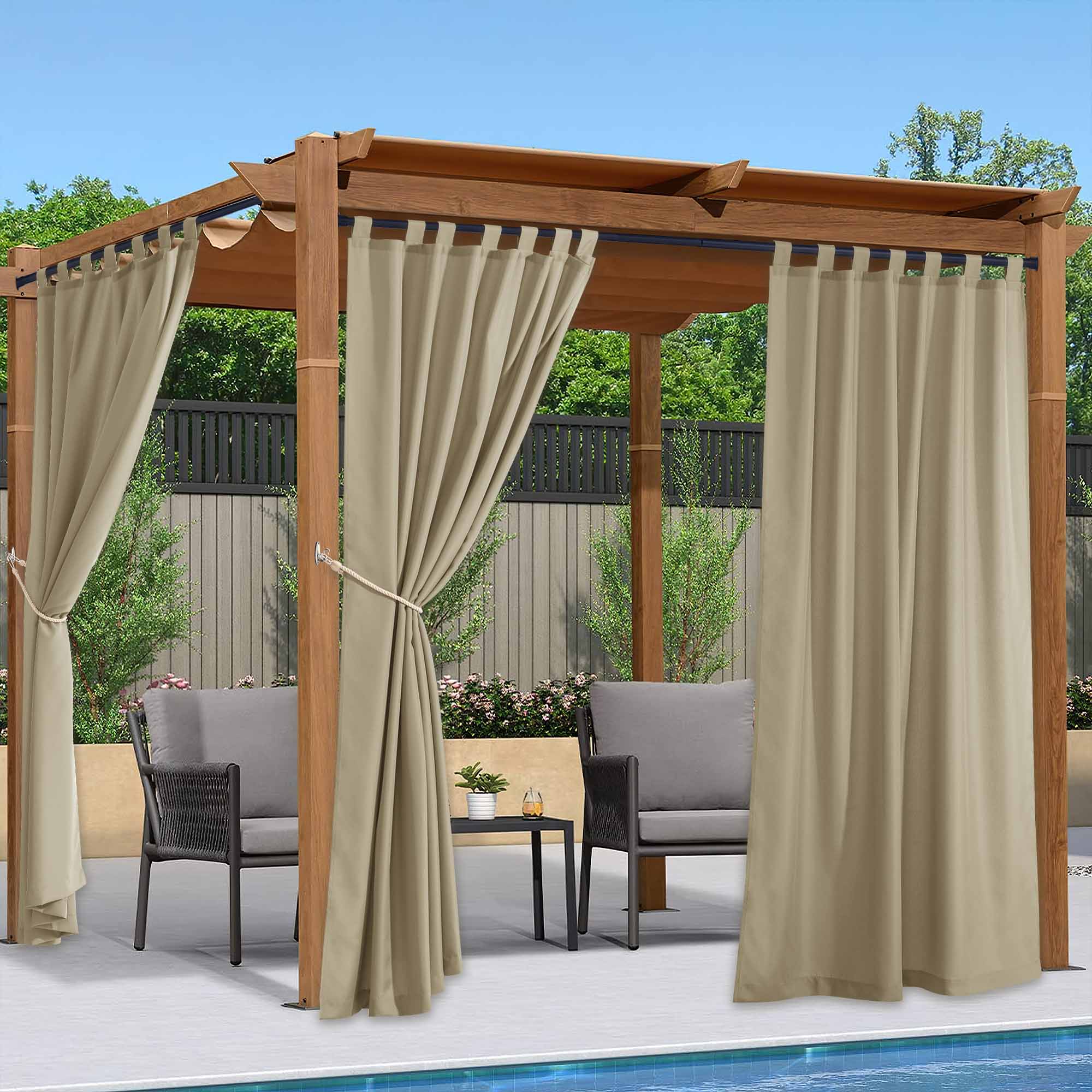 Beige waterproof outdoor canvas curtains tied back to a wooden pergola, providing shade for patio chairs by a swimming pool.