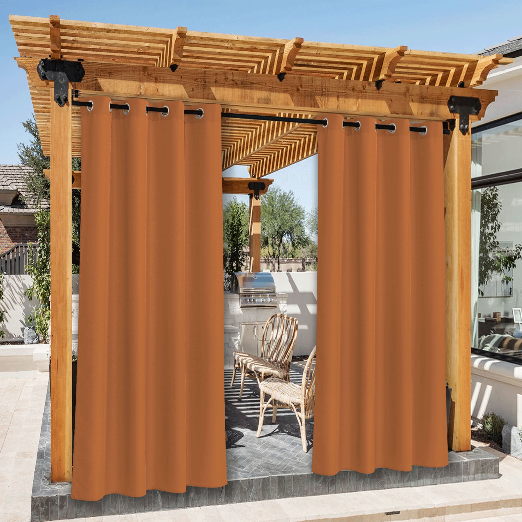 Orange waterproof canvas outdoor patio curtains hung on a wooden pergola, partially open to reveal a BBQ area and rattan chairs.