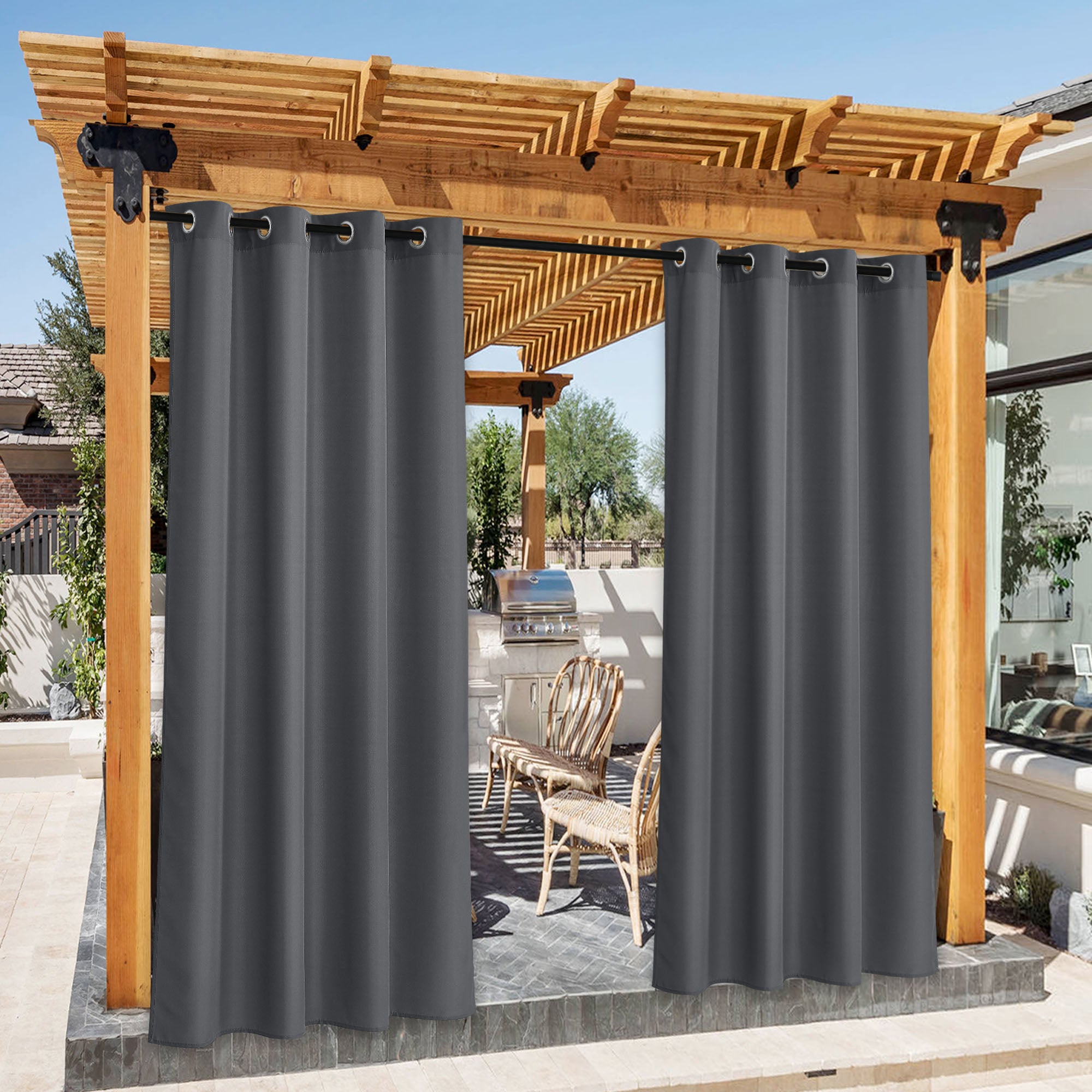 Dark gray waterproof outdoor canvas curtains with grommet tops on a wooden pergola, partially open to reveal a patio BBQ area