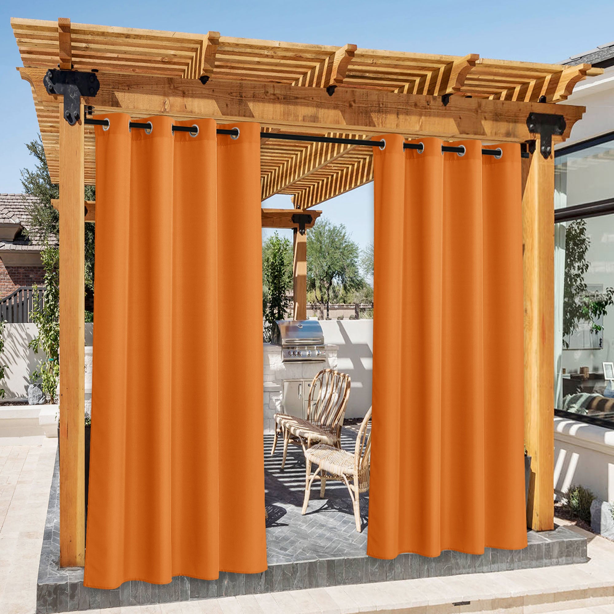 Orange waterproof canvas outdoor curtains with grommets on a wooden pergola, partially open showing a patio BBQ area.