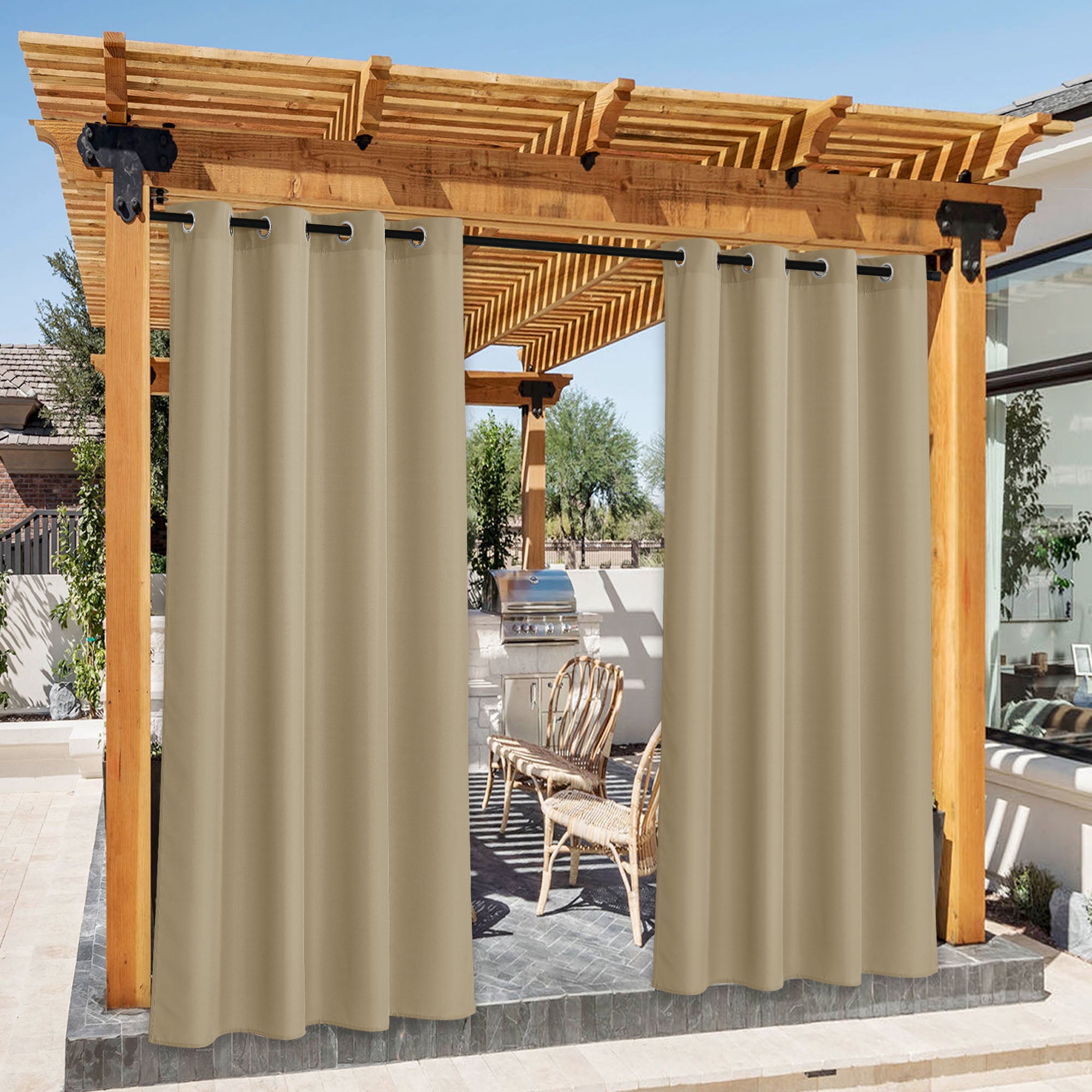 Two beige waterproof canvas outdoor curtains hanging under a wooden pergola, partially open to reveal a patio with grill.