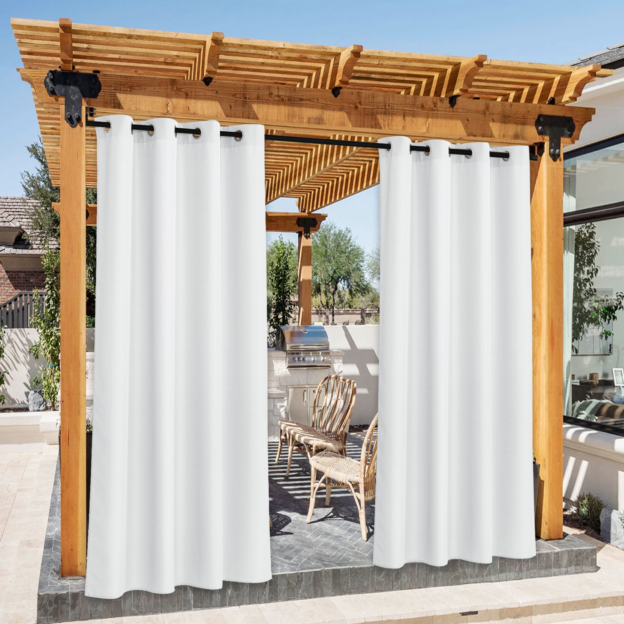 White grommet top waterproof outdoor curtains hanging from a black rod under a wooden pergola, with an outdoor kitchen view.