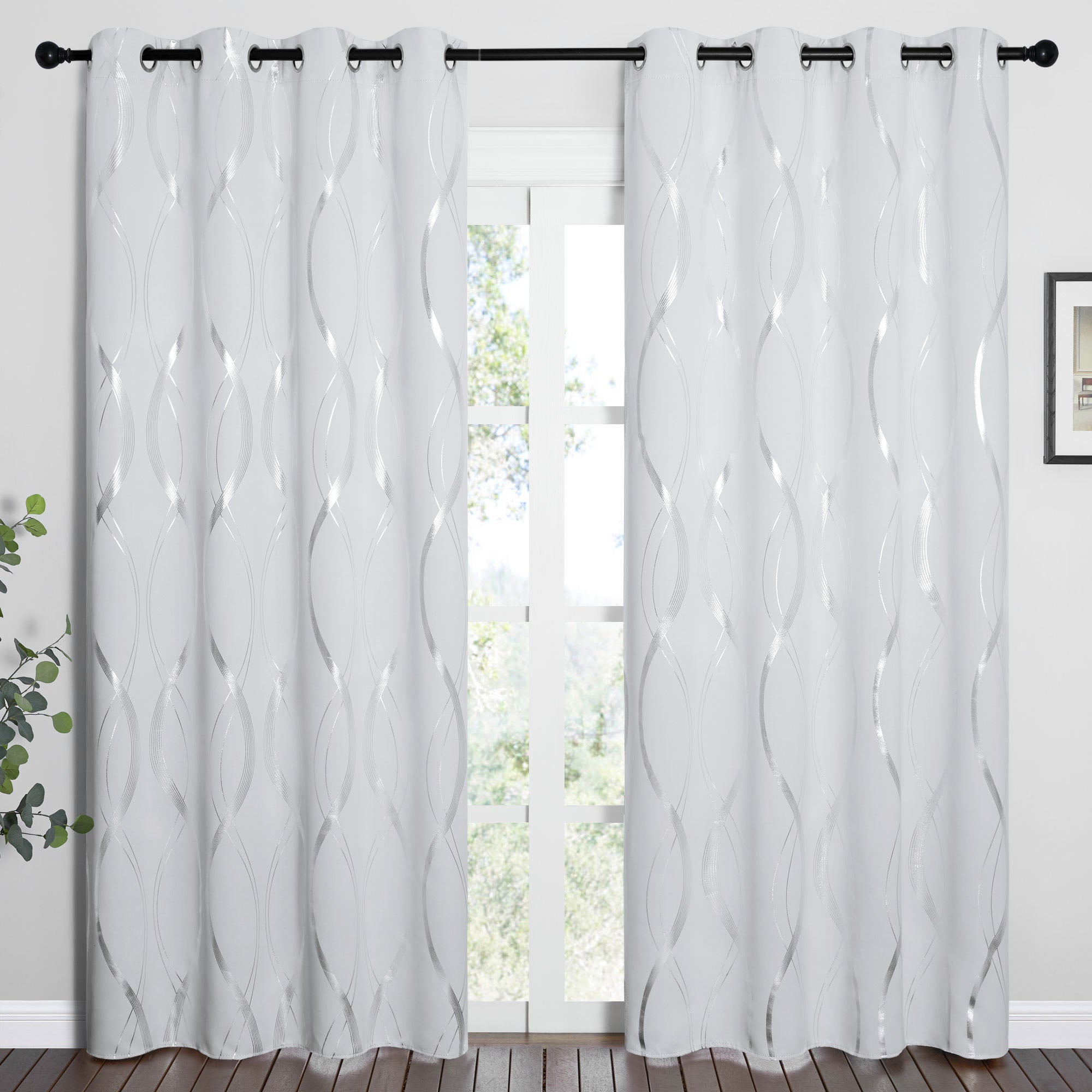 Pair of white wave line blackout curtains with silver pattern and grommets, hanging on a black rod in front of a window.