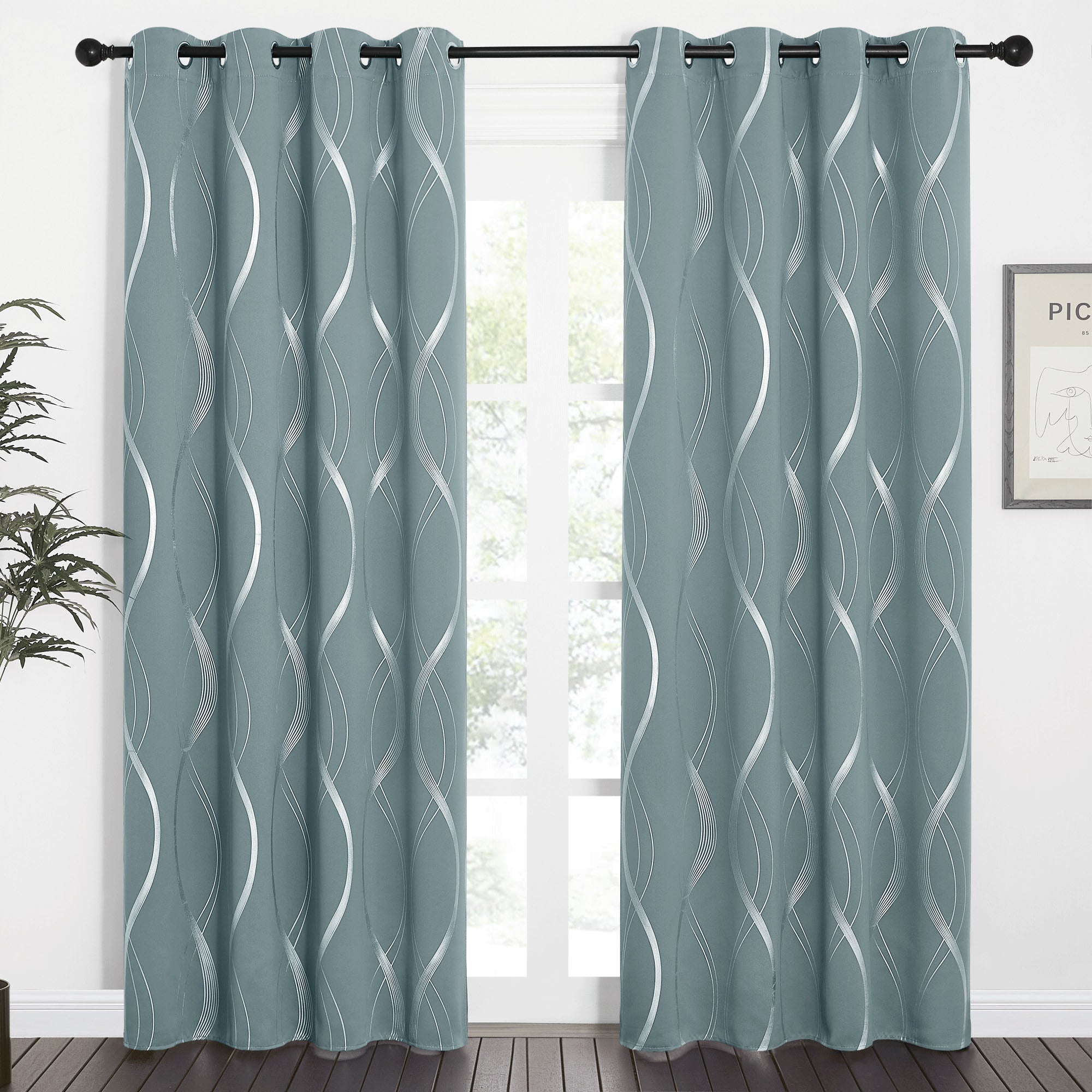 Teal wave line blackout curtains with silver patterns and grommet tops, hung on a black rod in front of a window.