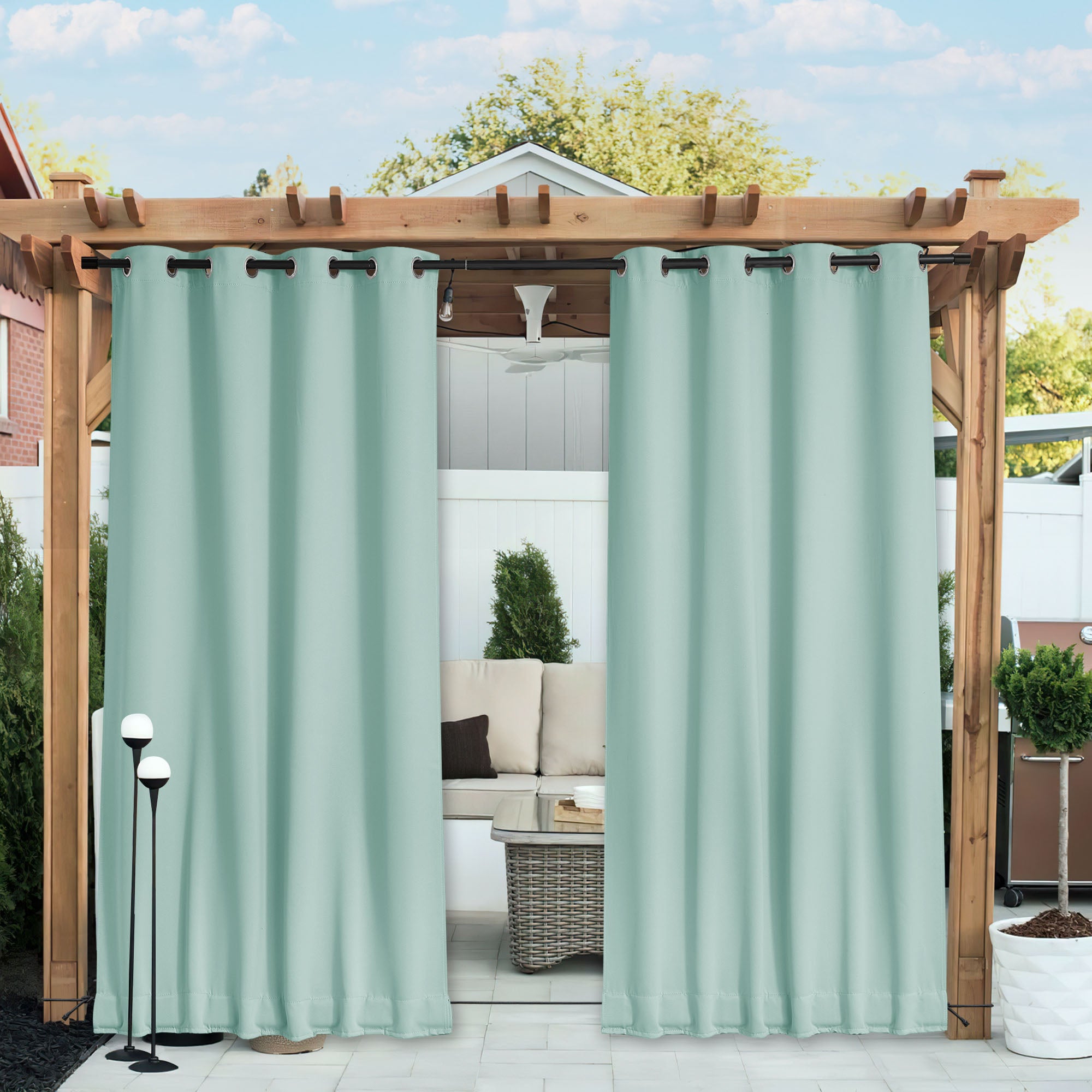 Light blue waterproof blackout outdoor curtains hung on a patio pergola, partially closed to shade a comfortable outdoor seating area.
