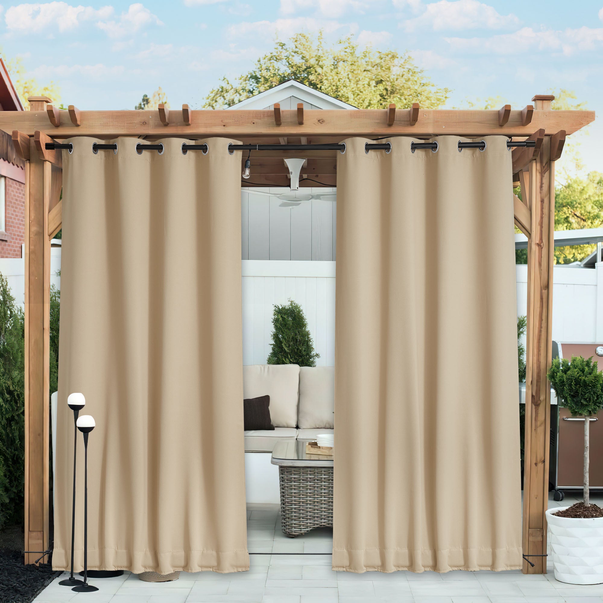 Tan waterproof blackout outdoor curtains on a wooden pergola, partially open to reveal a private patio seating area.