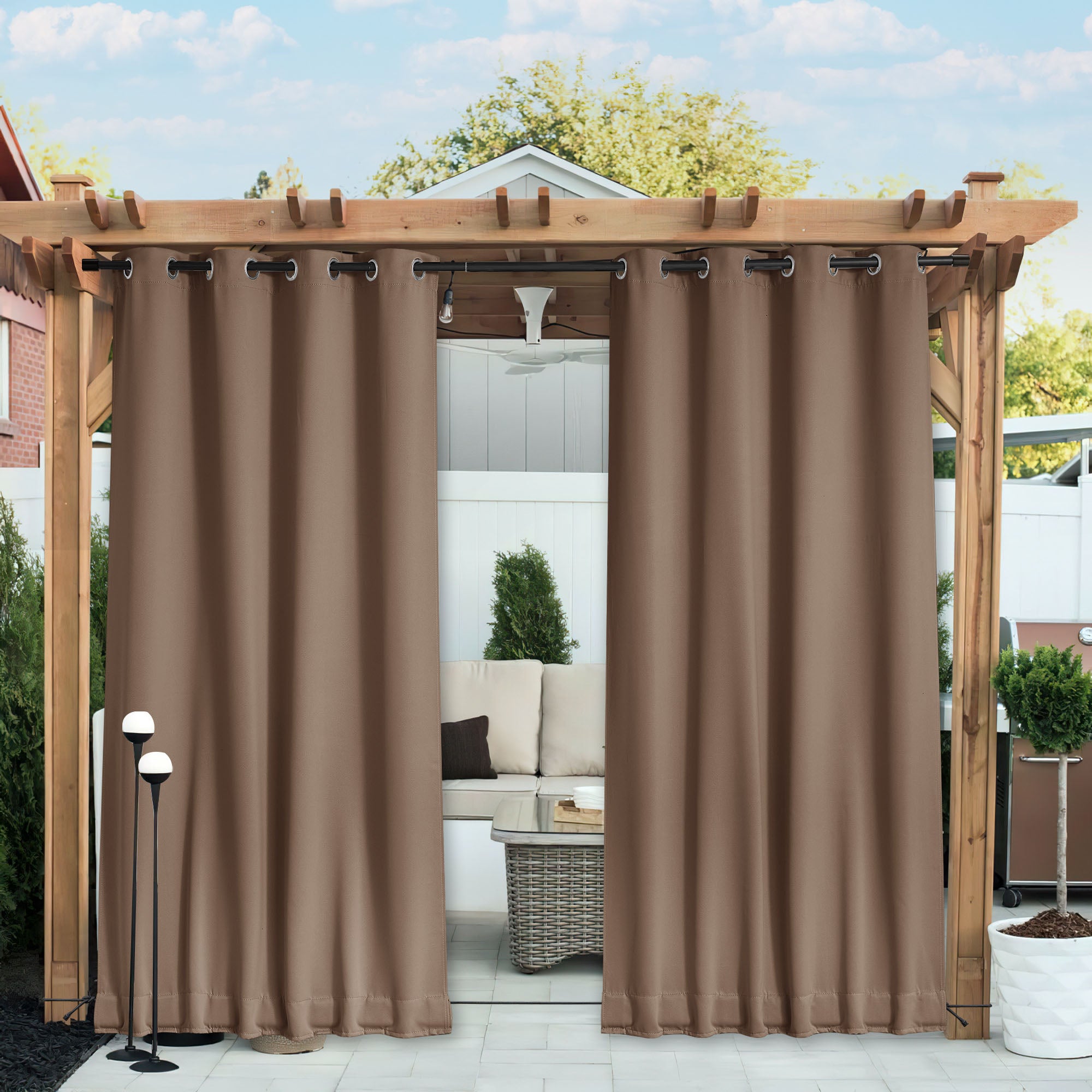Brown waterproof blackout outdoor curtains with grommets on a wooden pergola, partially open to a cozy patio seating area.