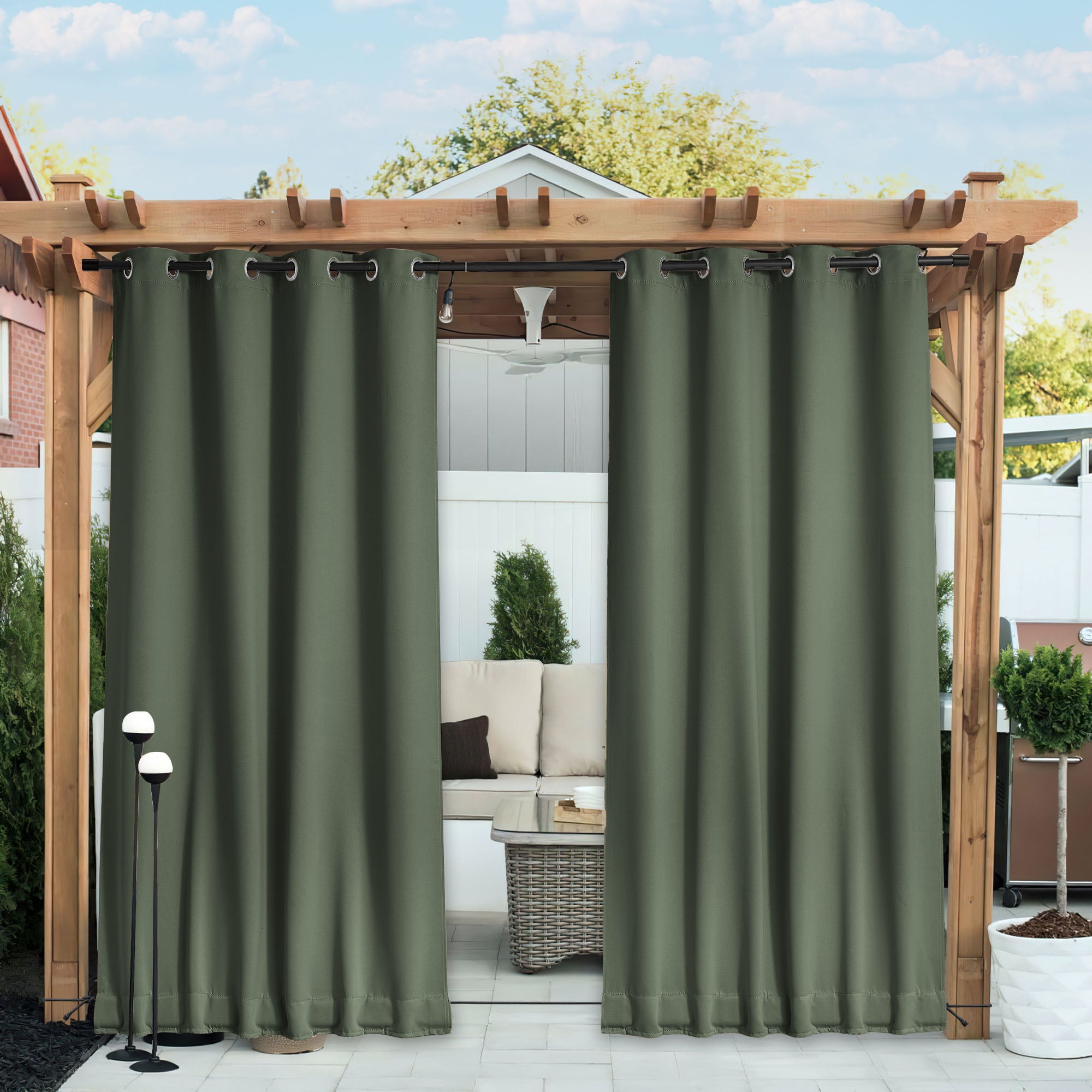 Olive green waterproof blackout outdoor curtains hanging from a wooden pergola, partially open to reveal a patio seating area.